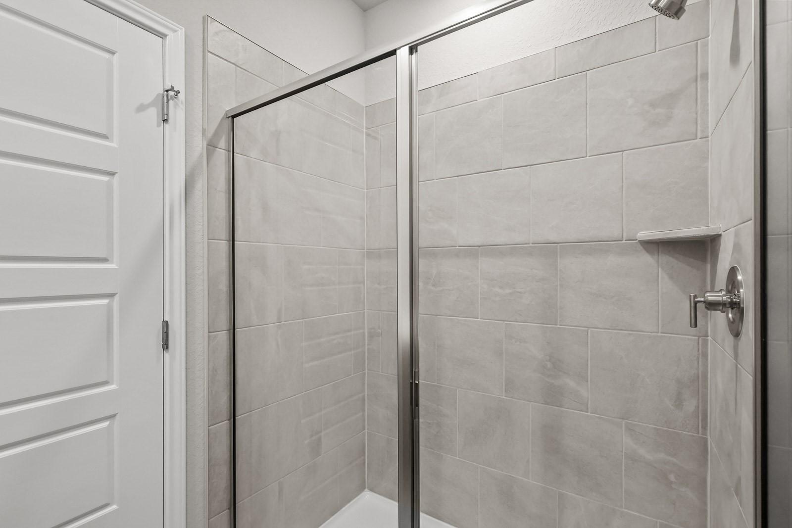 Modern walk-in shower with light grey tile surround in a Davidson Homes The Frio G floor plan in Heartland, Texas.