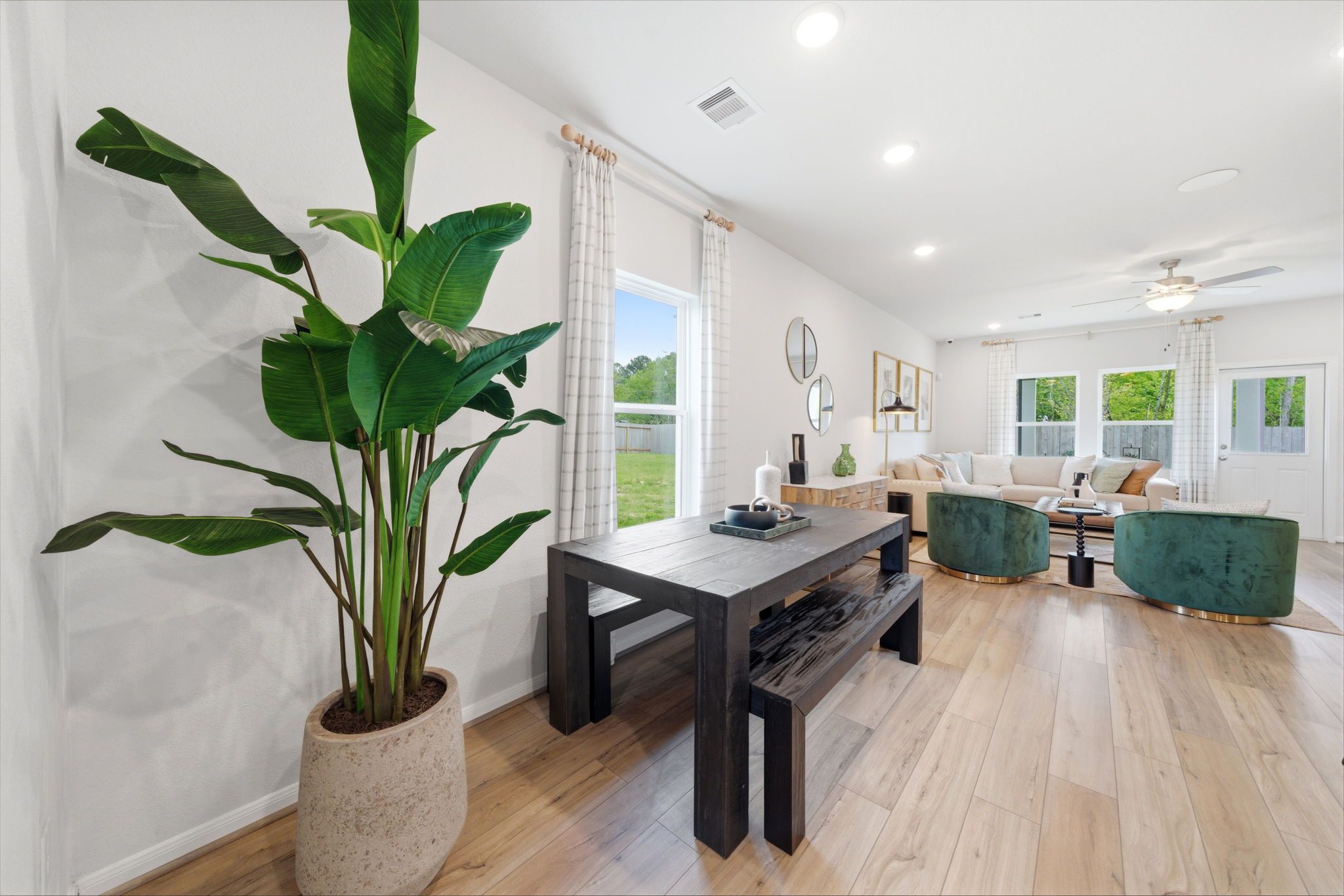 Modern dining area at Caney Creek Place in Conroe Texas with wooden table green velvet chairs hardwood floors and large potted plant