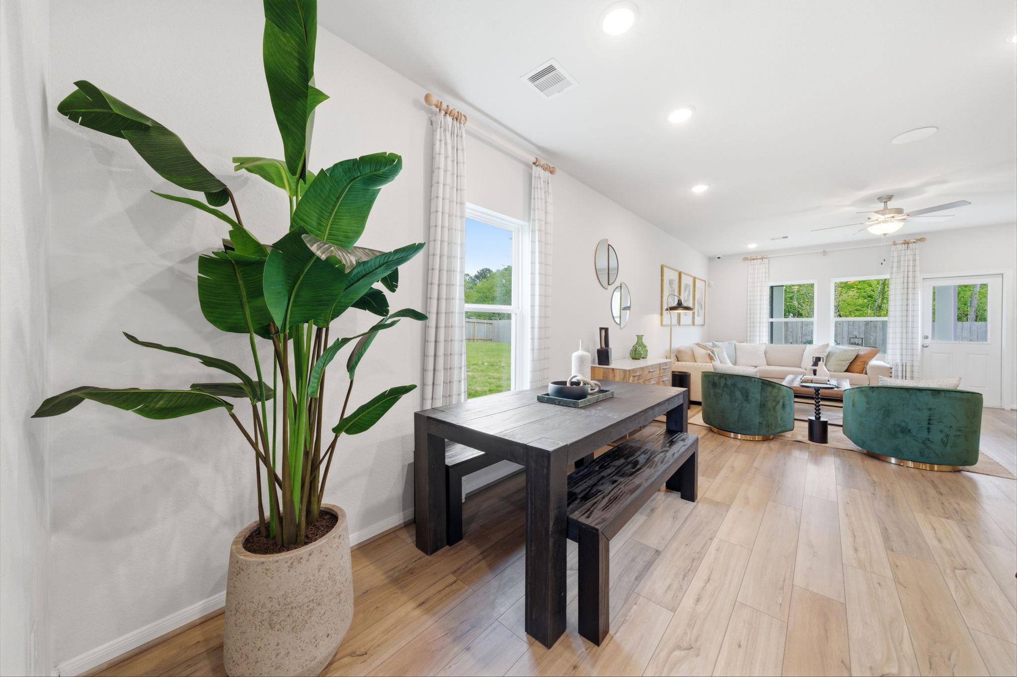 Modern dining area at Caney Creek Place in Conroe Texas with wooden table green velvet chairs hardwood floors and large potted plant