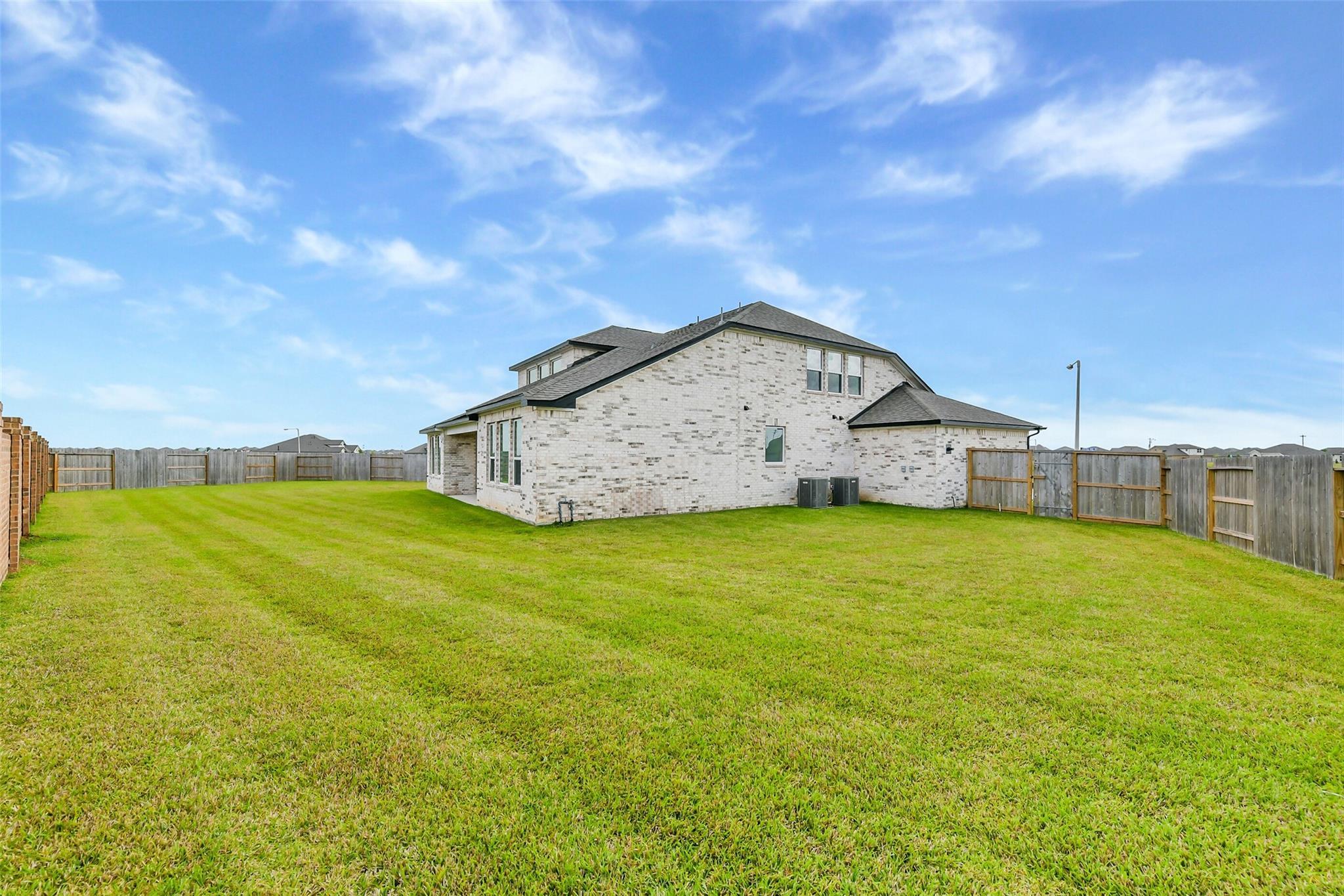 Two-story white brick home exterior with expansive green backyard, wooden fence, and AC units in Lago Mar, Texas City, Texas - Davidson Homes The Victoria A