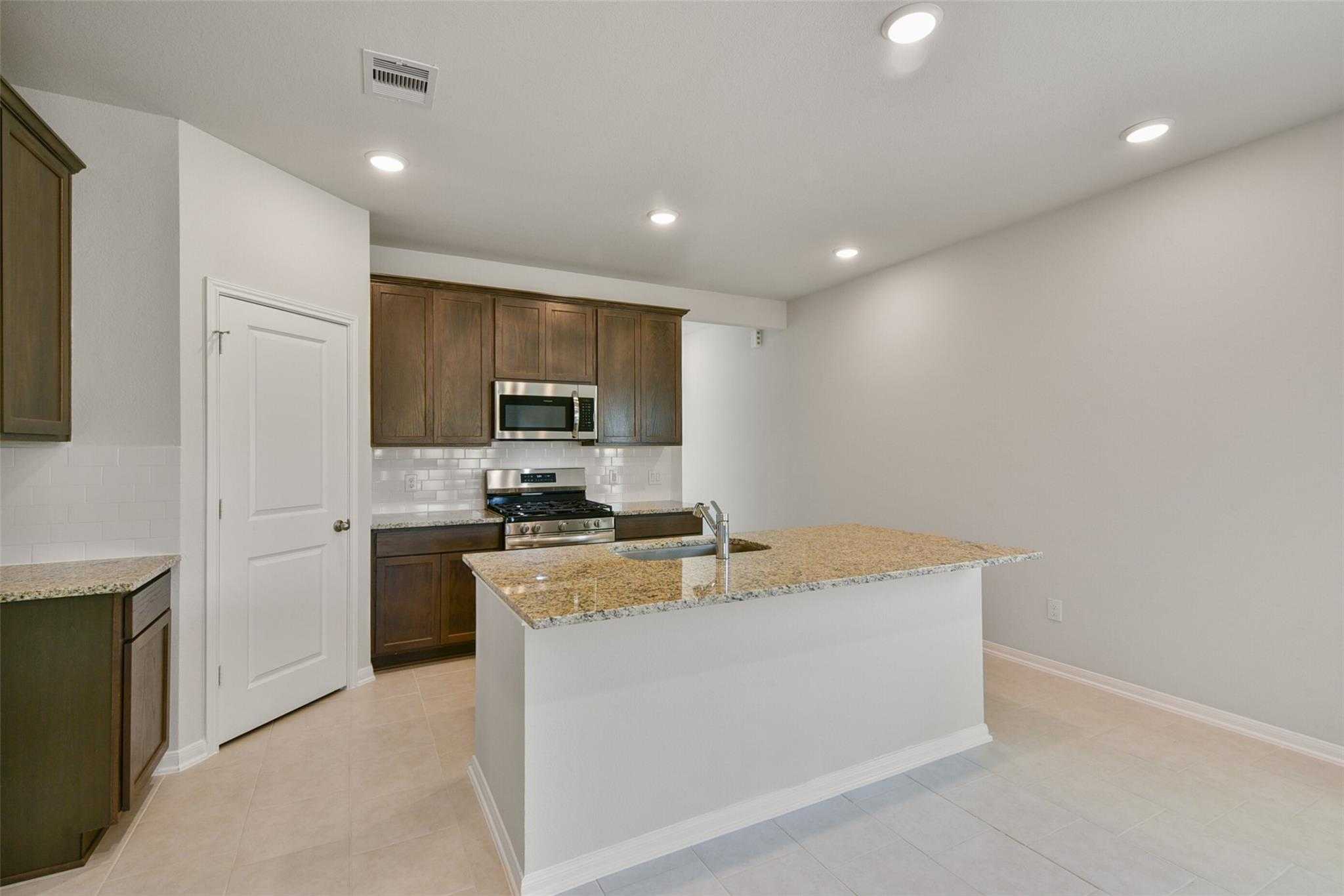Modern kitchen featuring granite island, stainless steel appliances, and wood cabinets in Davidson Homes The Sabine E, Dayton, Texas