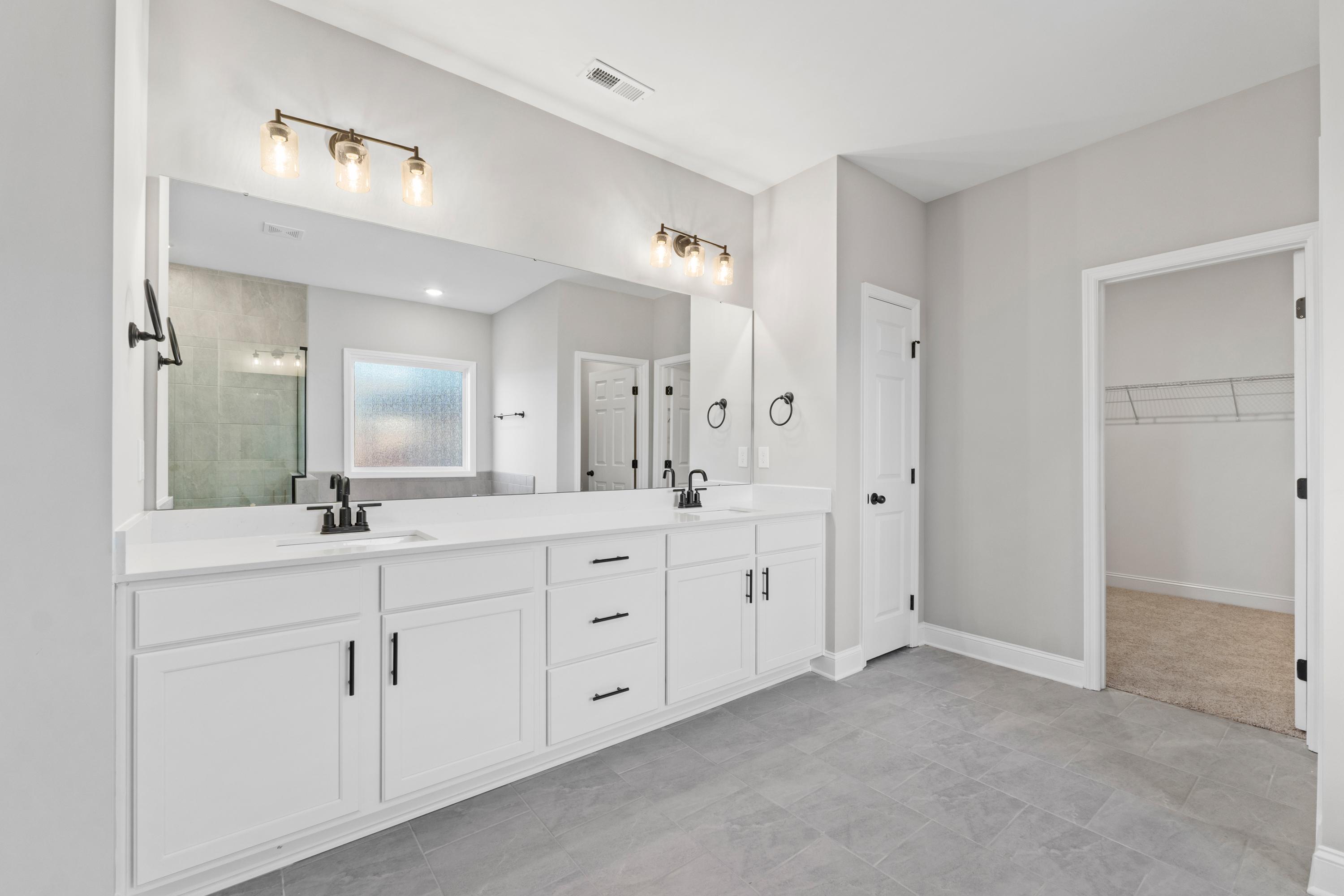 Spacious master bathroom in The Valencia featuring white double vanity, large mirrors, walk-in shower, and gray tile floor