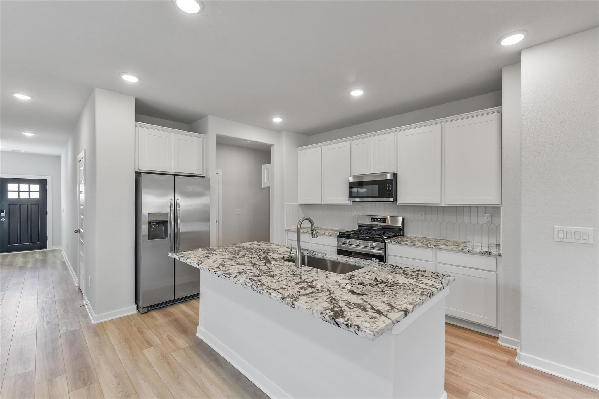 Modern white kitchen with granite island sink, stainless appliances, open to hallway in The Brazos F, Davidson Homes, Magnolia TX