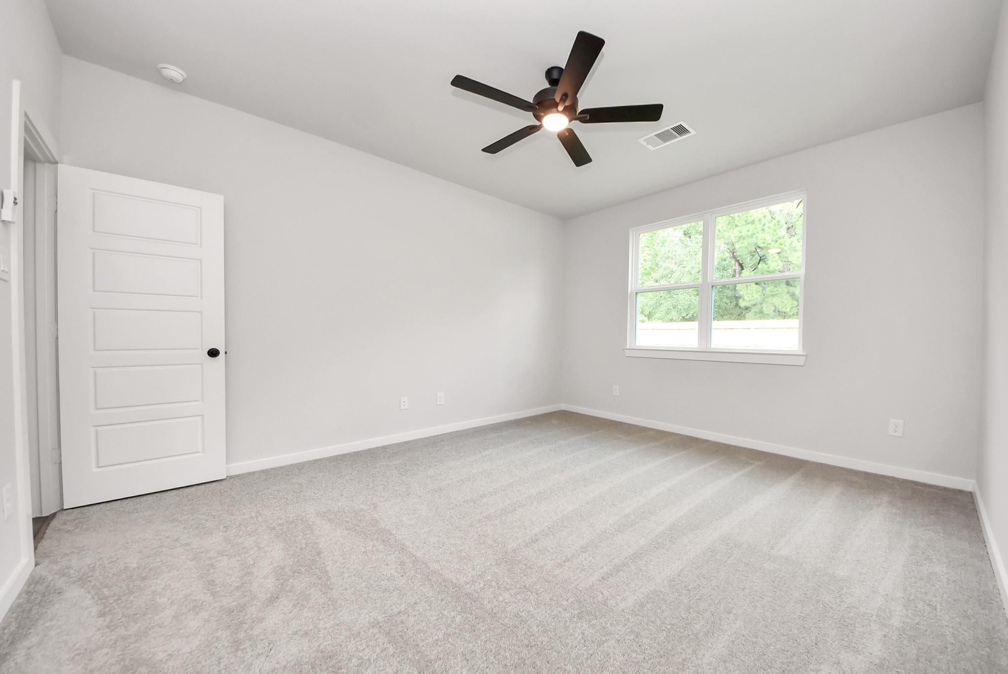 Bright, carpeted bedroom with ceiling fan in The Daphne F floor plan at Sundance Cove, Crosby, Texas.