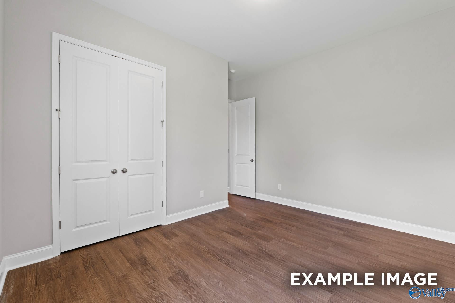 Spacious bedroom featuring white double closet doors, light gray walls, and hardwood floors in Evermore Homes The Arcadia, Owens Cross Roads, Alabama