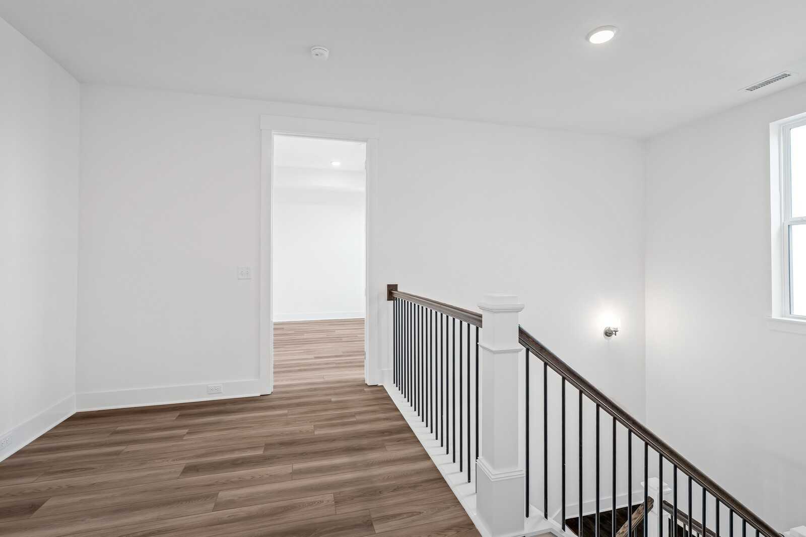 Bright upstairs hallway with hardwood floors, white walls, black metal railing, and open doorway in The Alston A floor plan, Murfreesboro, TN