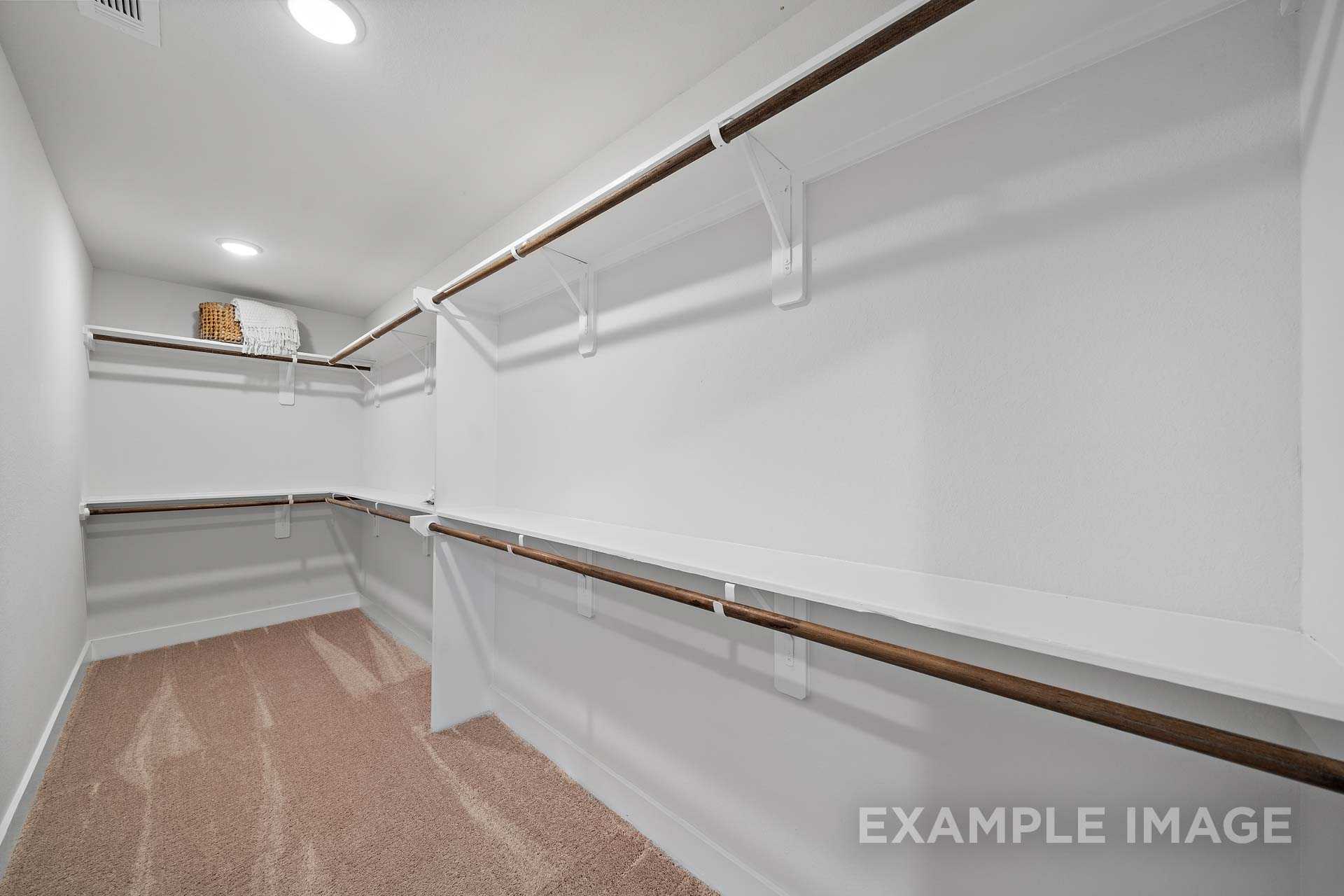 Spacious walk-in closet in The Rose B master suite featuring white walls, wooden rods, shelves, beige carpet, and recessed lighting