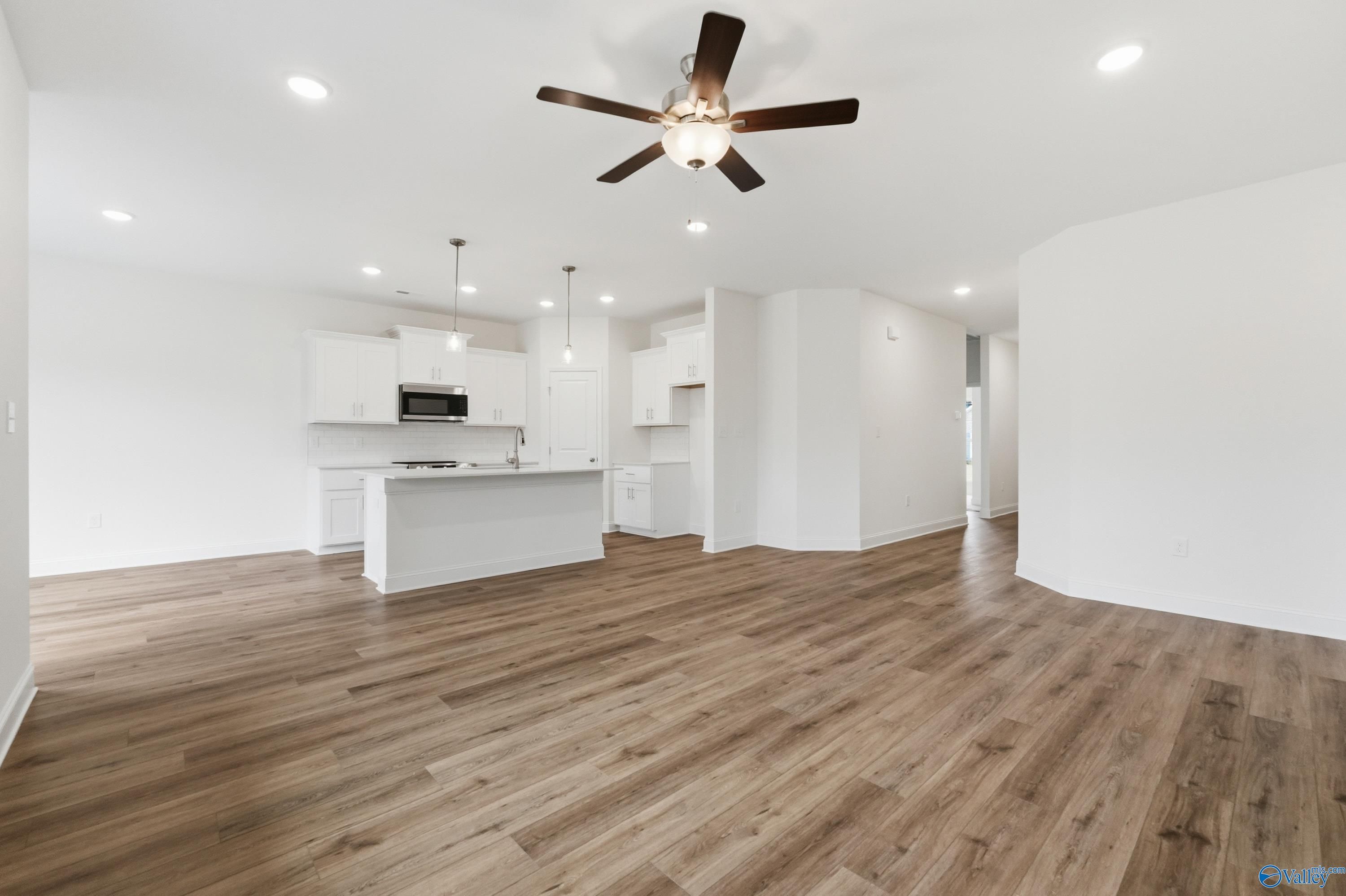 Spacious open kitchen with white cabinets, large island, hardwood floors, and ceiling fan in The Asheville C by Davidson Homes, Meridianville, AL