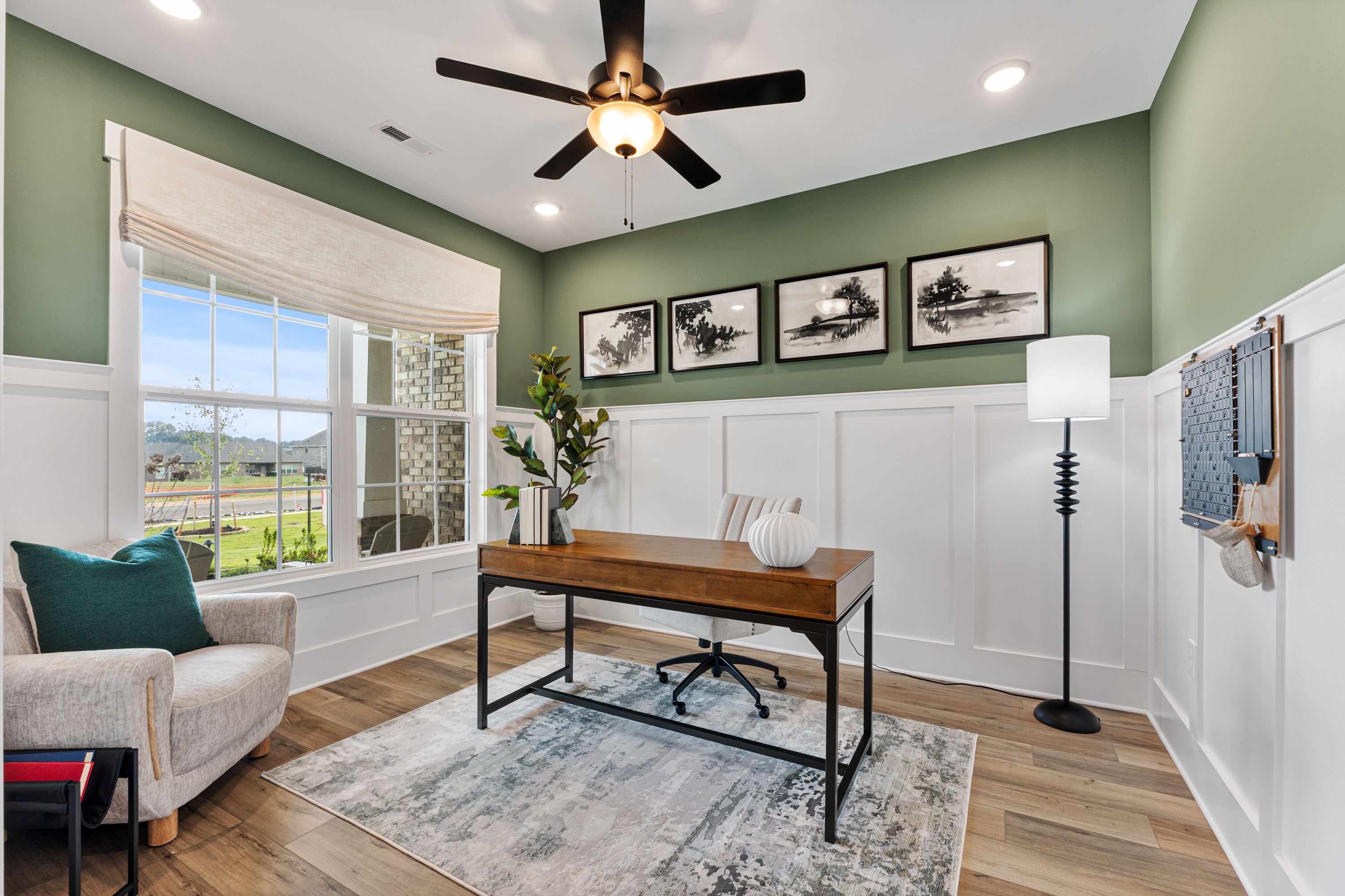 Modern home office at River Road Estates in Decatur, Alabama with sage green walls, wooden desk, large window, and potted plant