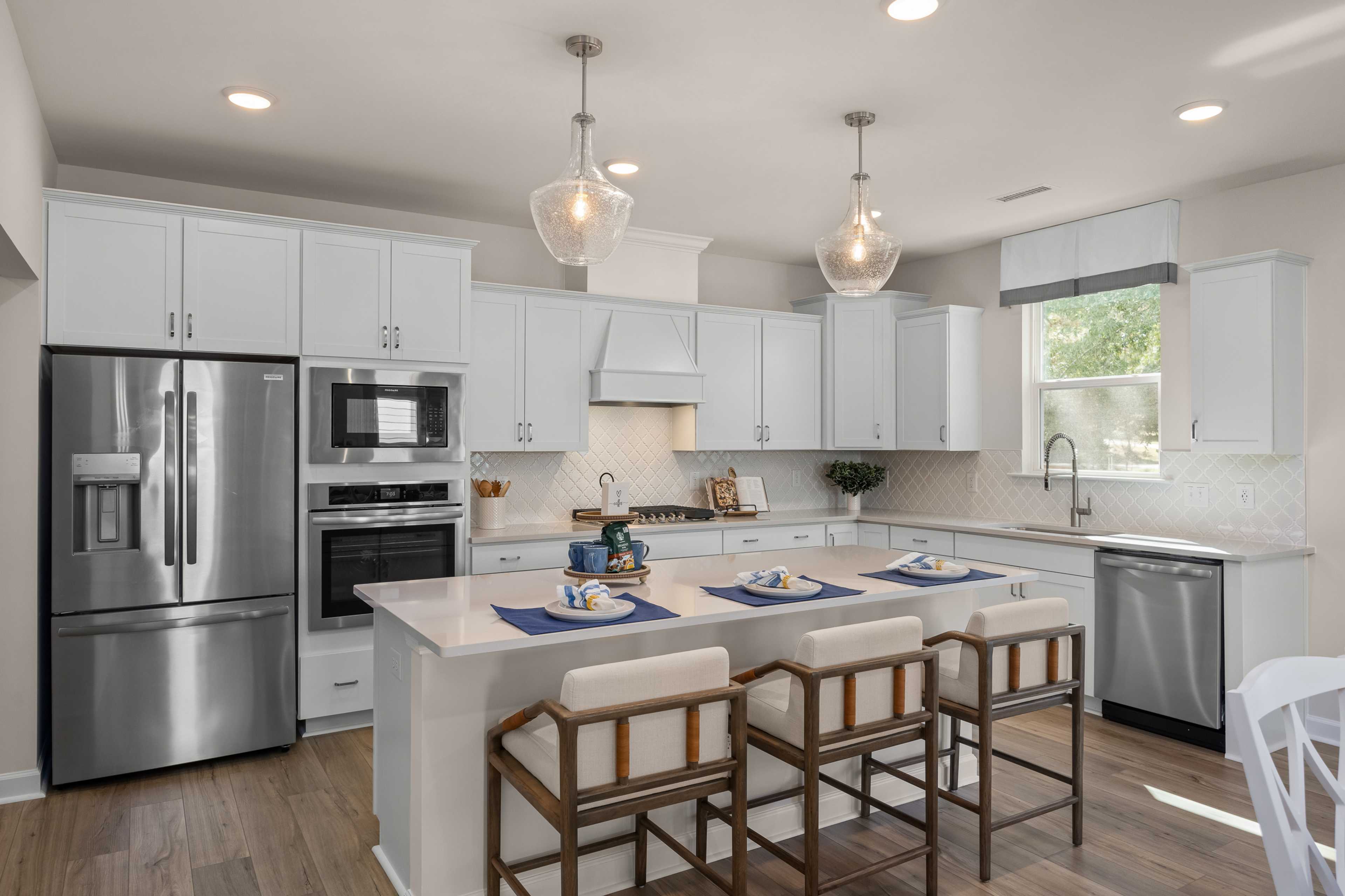 Spacious modern kitchen with white cabinets, stainless steel appliances, island bar seating, and hardwood floors at Sage on North Main, Wake Forest NC