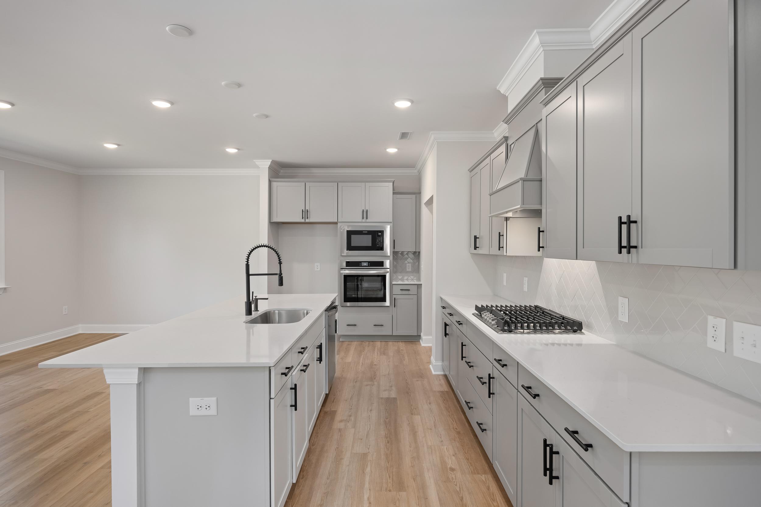 Beech A gourmet kitchen with gray shaker cabinets, white quartz island, double wall ovens, gas cooktop, farmhouse sink