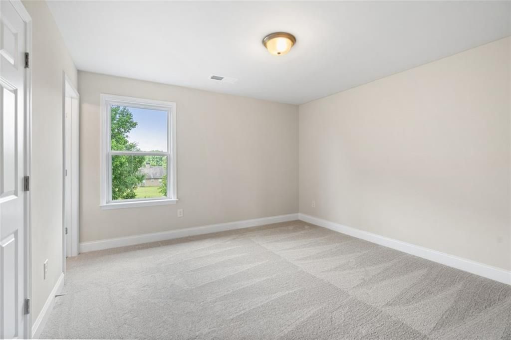 Bright secondary bedroom with beige walls, gray carpet, and window overlooking trees in Davidson Homes The Willow B, Hoschton, Georgia