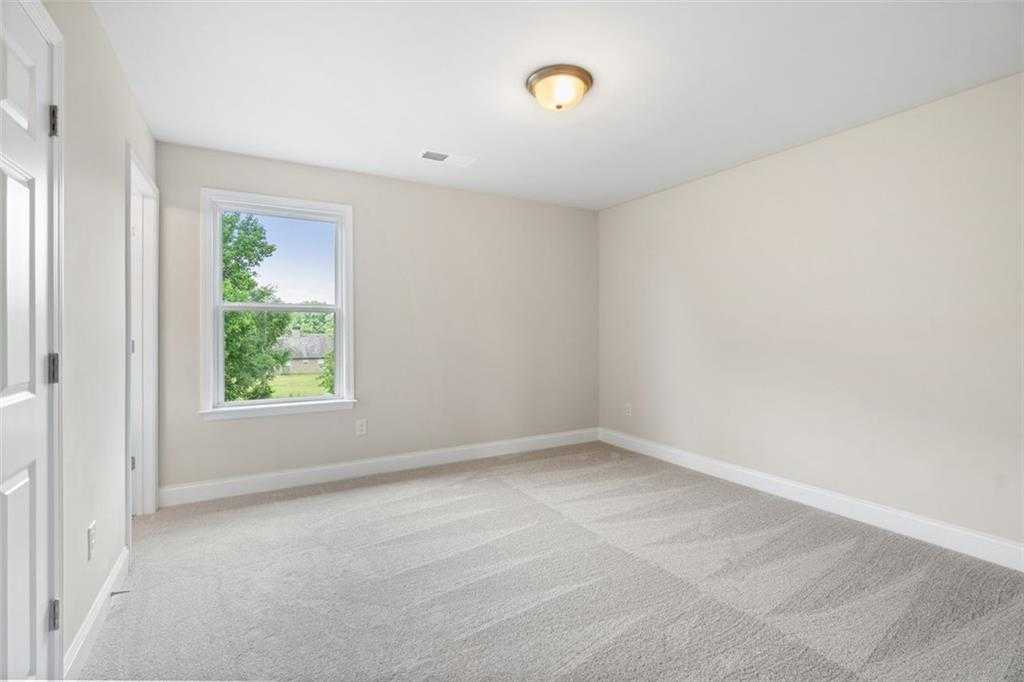Bright secondary bedroom with beige walls, gray carpet, and window overlooking trees in Davidson Homes The Willow B, Hoschton, Georgia