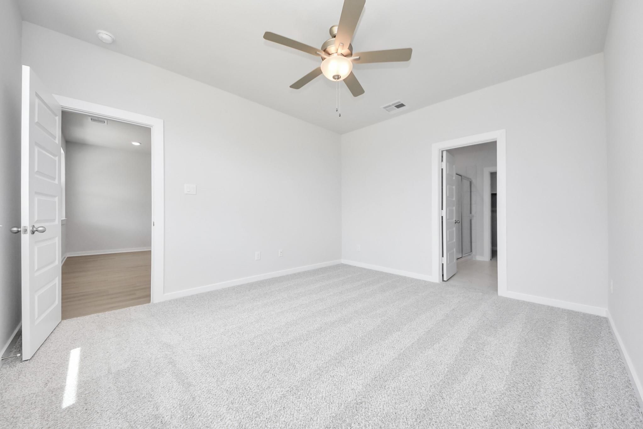 Spacious bedroom with plush carpet and ceiling fan in The Blanco F floor plan at Spring Branch Crossing, Conroe, Texas.