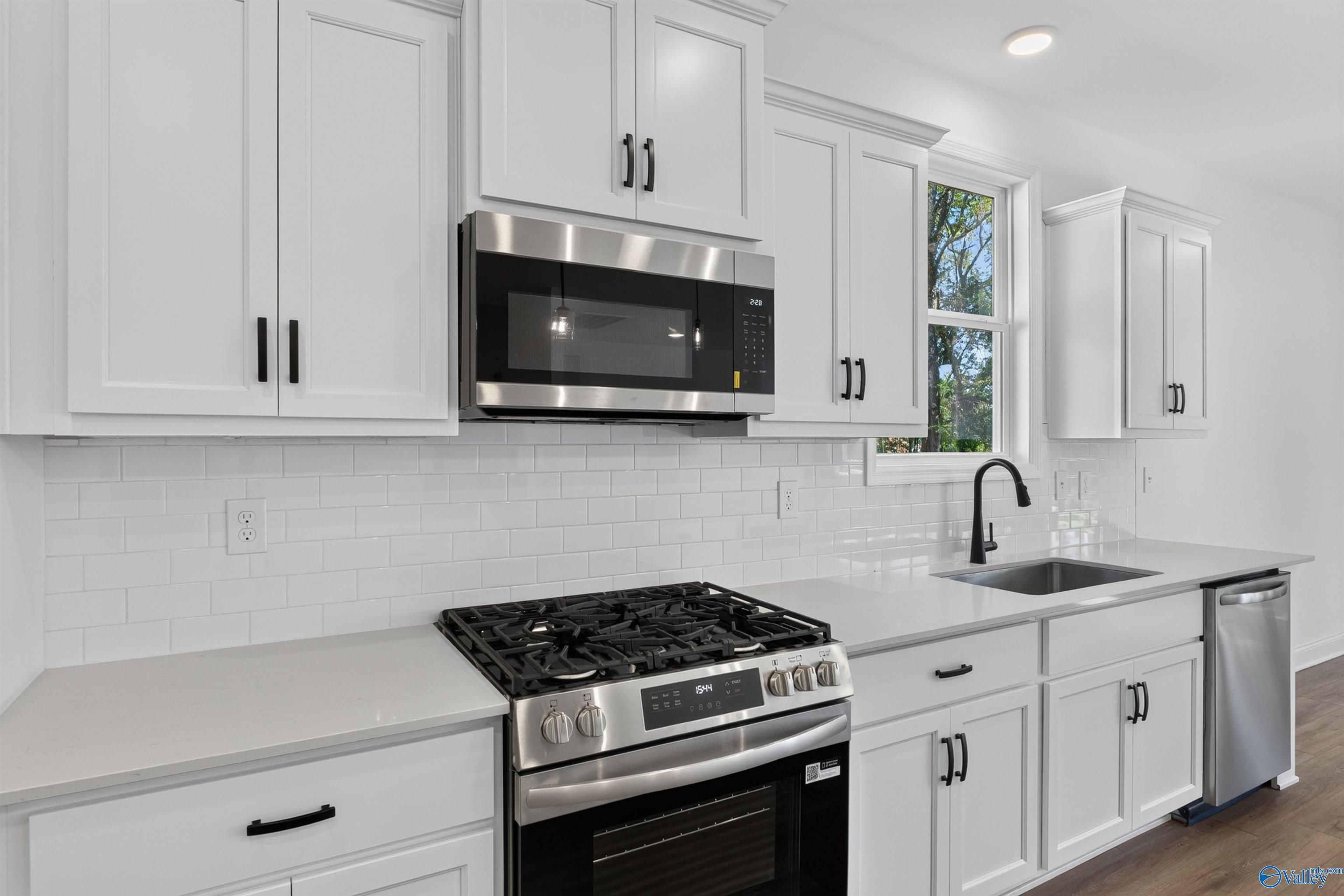 White shaker kitchen with gas range, stainless microwave, subway tile backsplash, and quartz countertops in Davidson Homes Ashport L plan