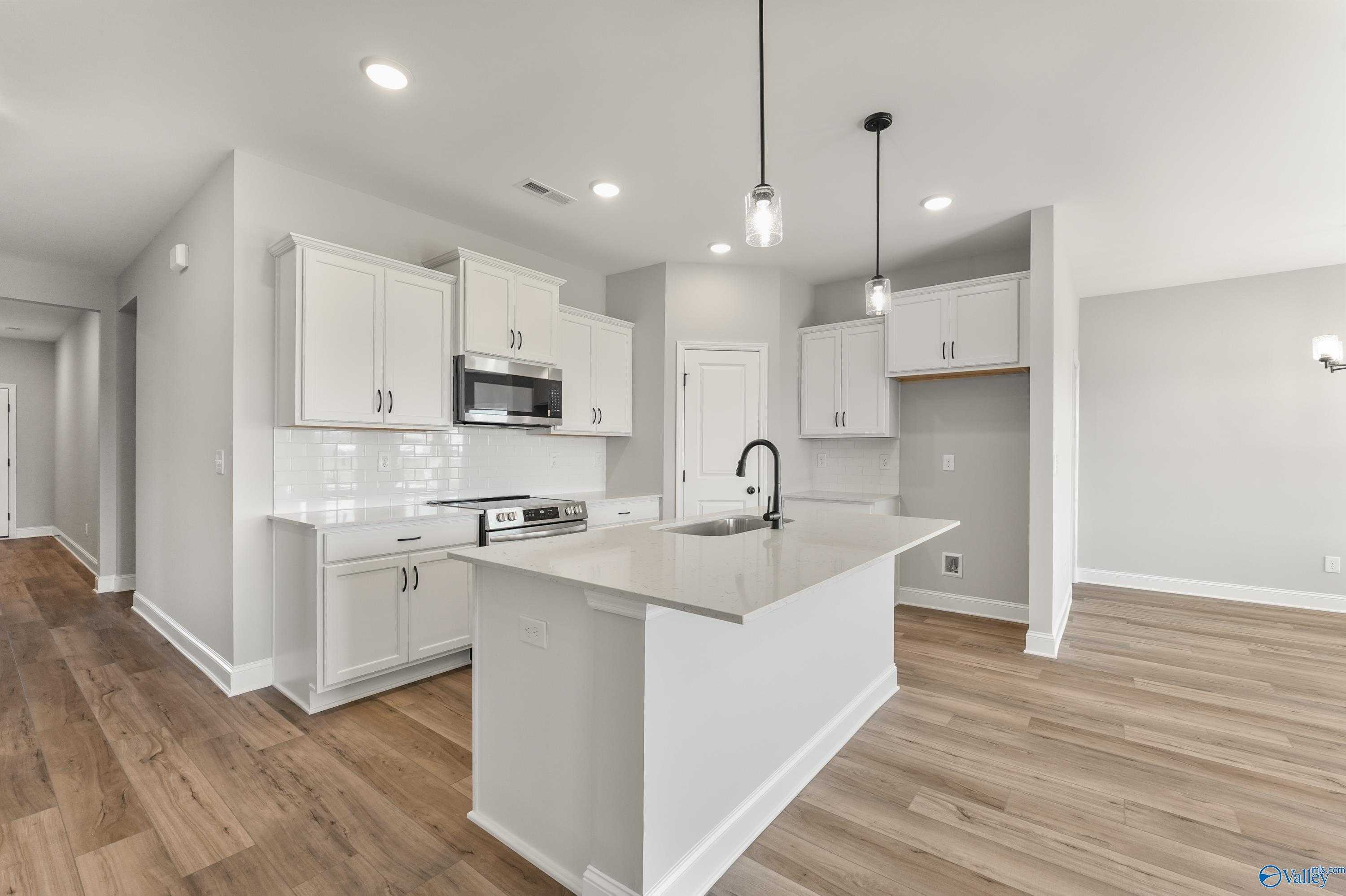 Modern white kitchen island with stainless appliances and hardwood floors in Davidson Homes The Daphne C, Hazel Green, AL