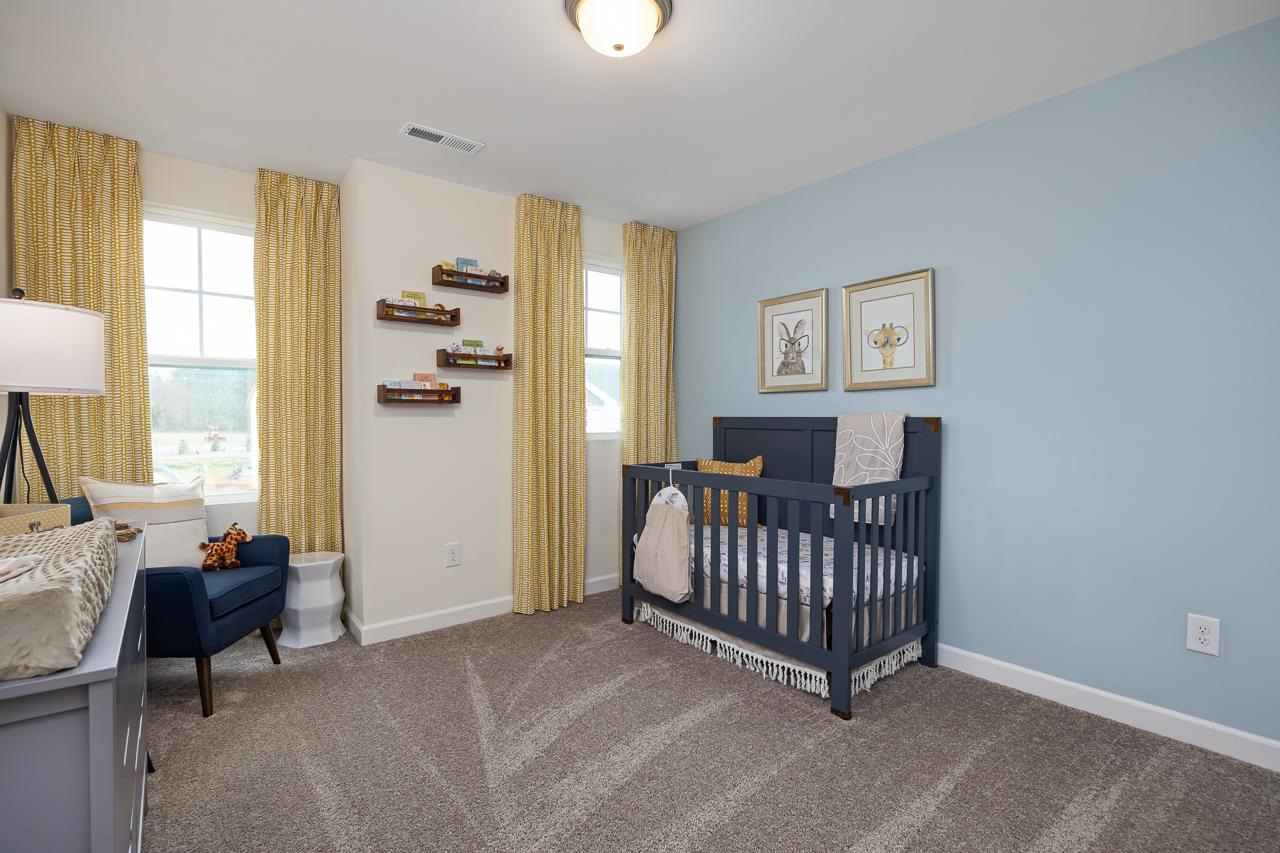 Cozy light blue nursery at Gregory Village Townhomes in Lillington NC with navy crib, yellow curtains, bookshelves, and armchair