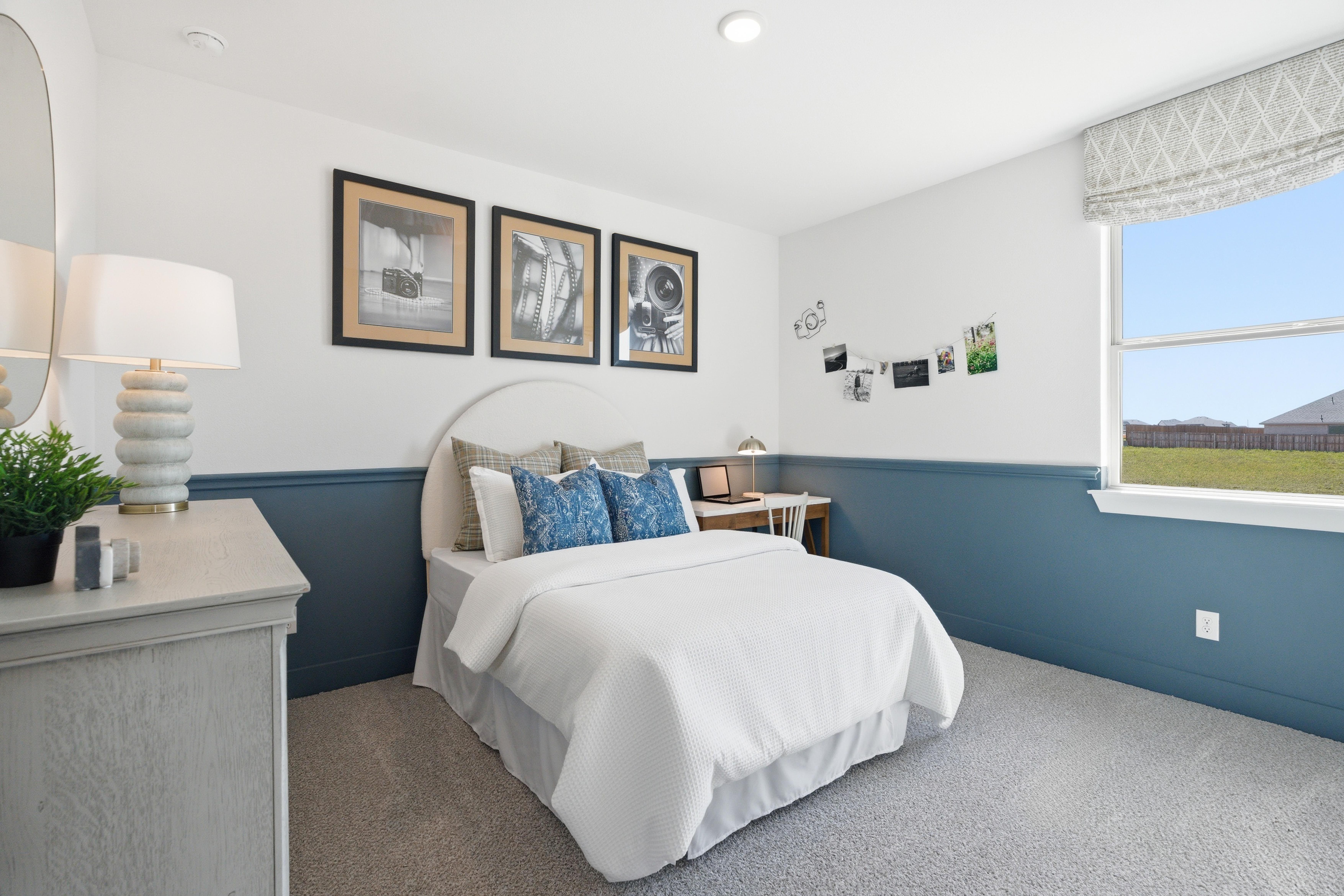 Cozy bedroom in Mercer Meadows Royse City TX with white bed blue pillows wainscoting nightstand lamp and window overlooking field