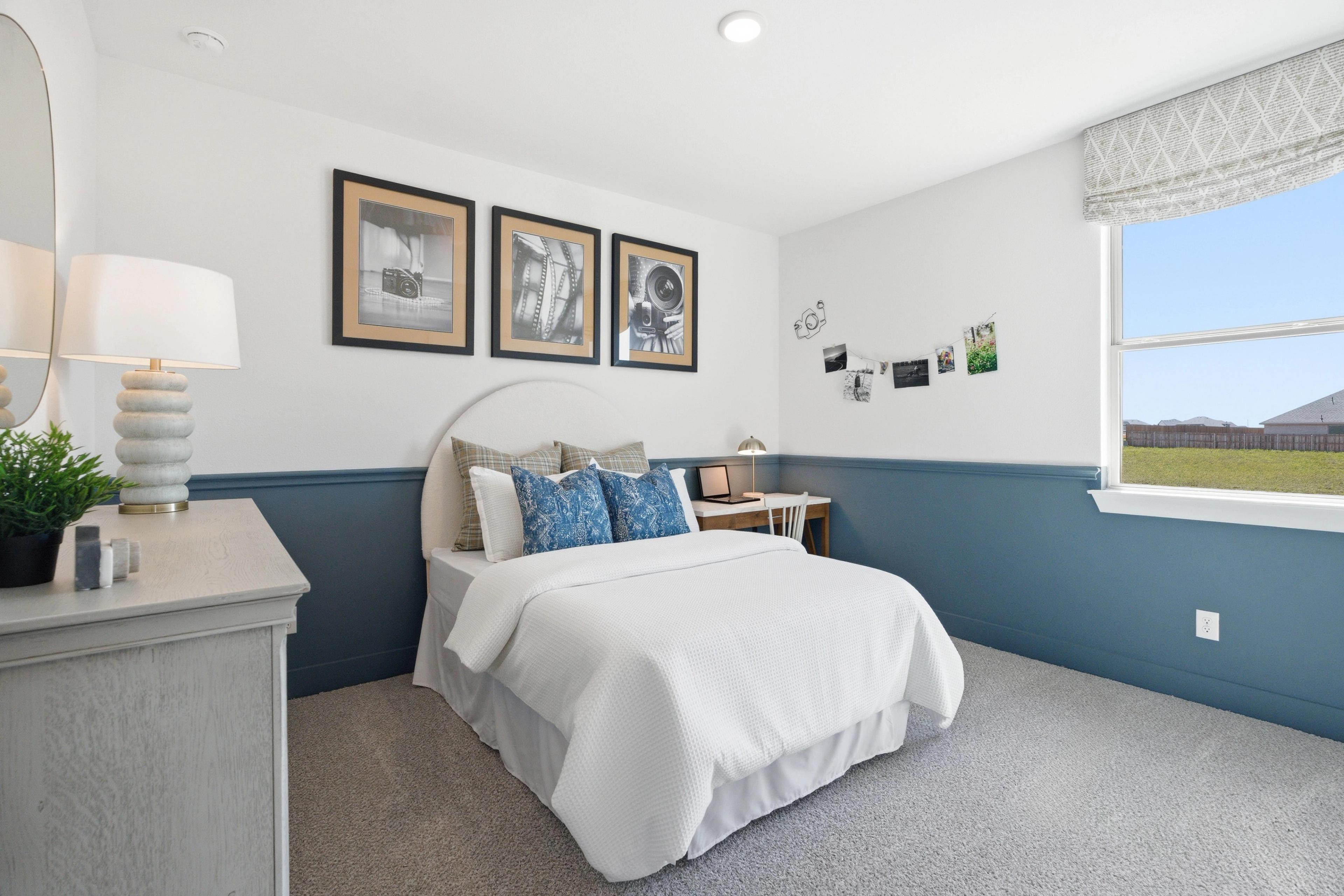 Cozy bedroom in Mercer Meadows Royse City TX with white bed blue pillows wainscoting nightstand lamp and window overlooking field