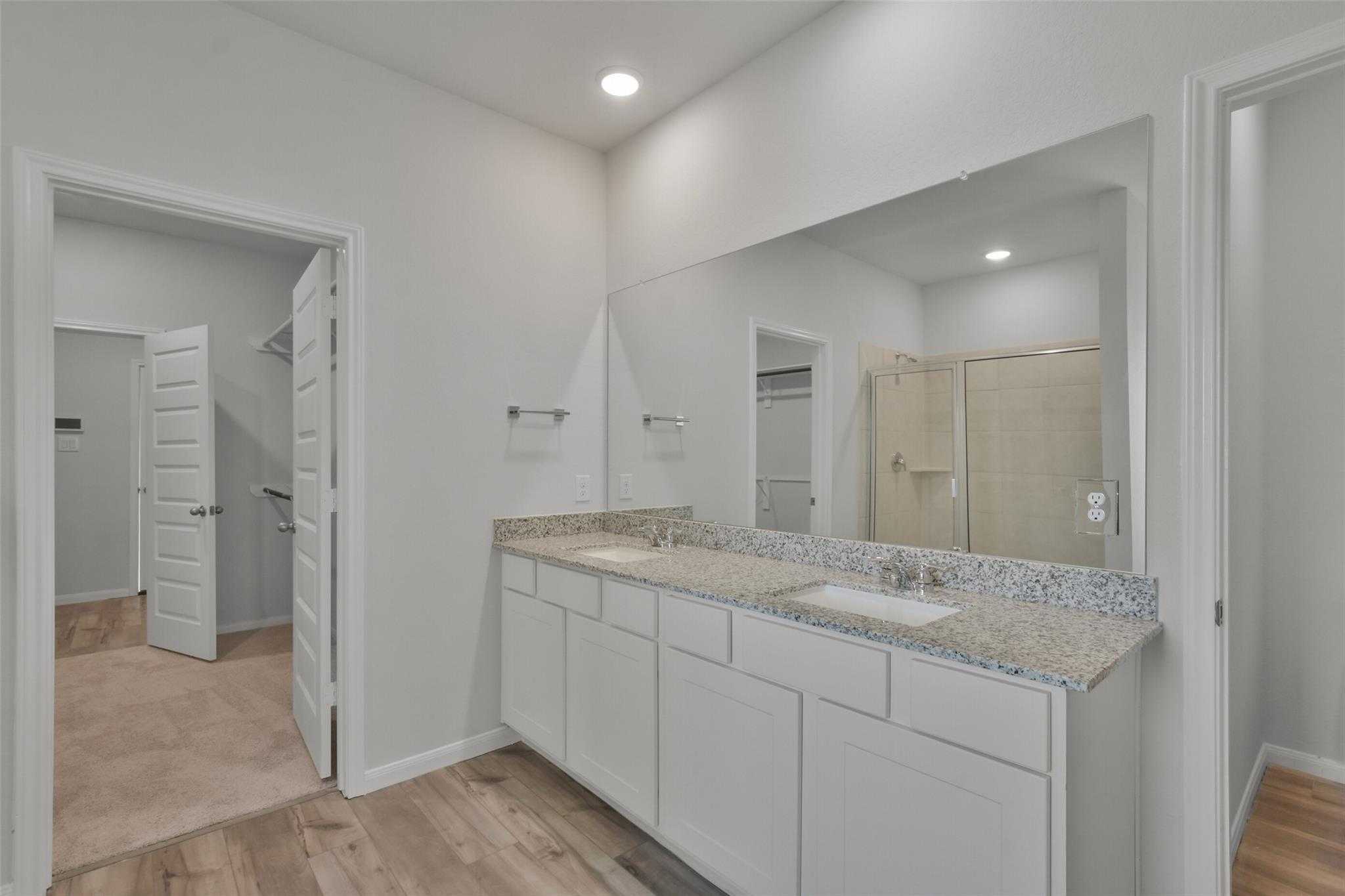 Modern master bathroom featuring double granite vanity, white cabinets, large mirror, and glass shower in Davidson Homes The Tierra A, Dayton, Texas