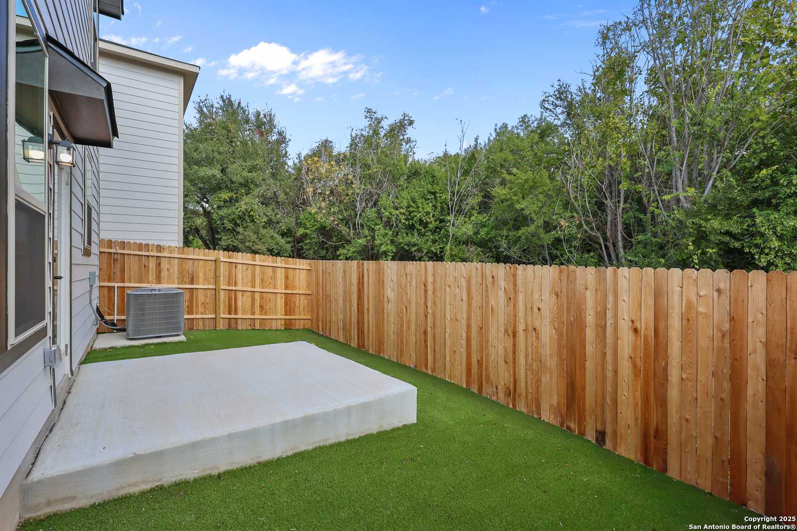 Private fenced backyard with lush artificial turf, concrete patio, and mature trees in Davidson Homes The Florence C, Cedar Heights, San Antonio