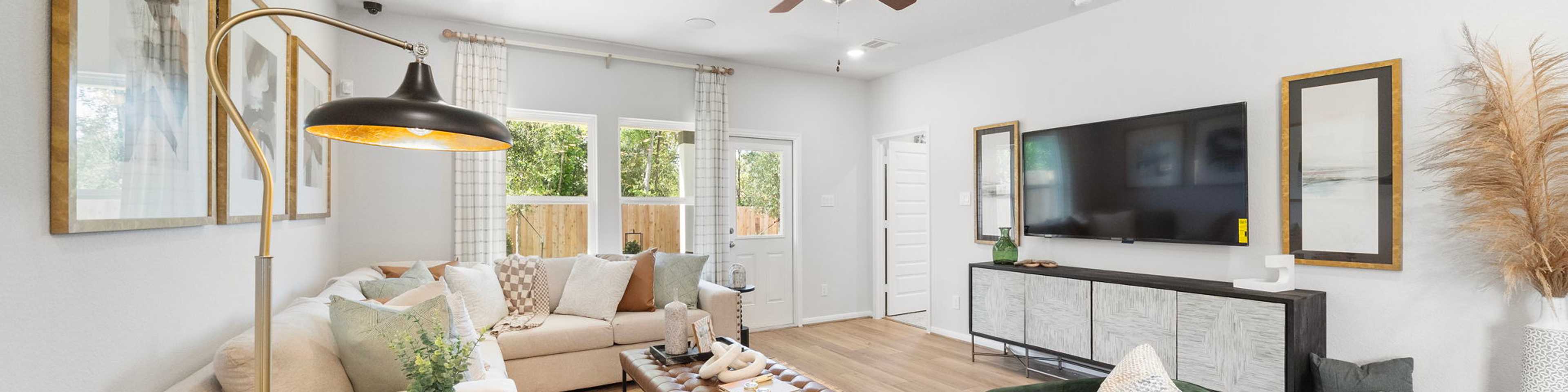 Spacious living room in Caney Creek Place Conroe TX with beige sectional sofa, emerald green velvet chairs, hardwood floors, ceiling fan, and modern art