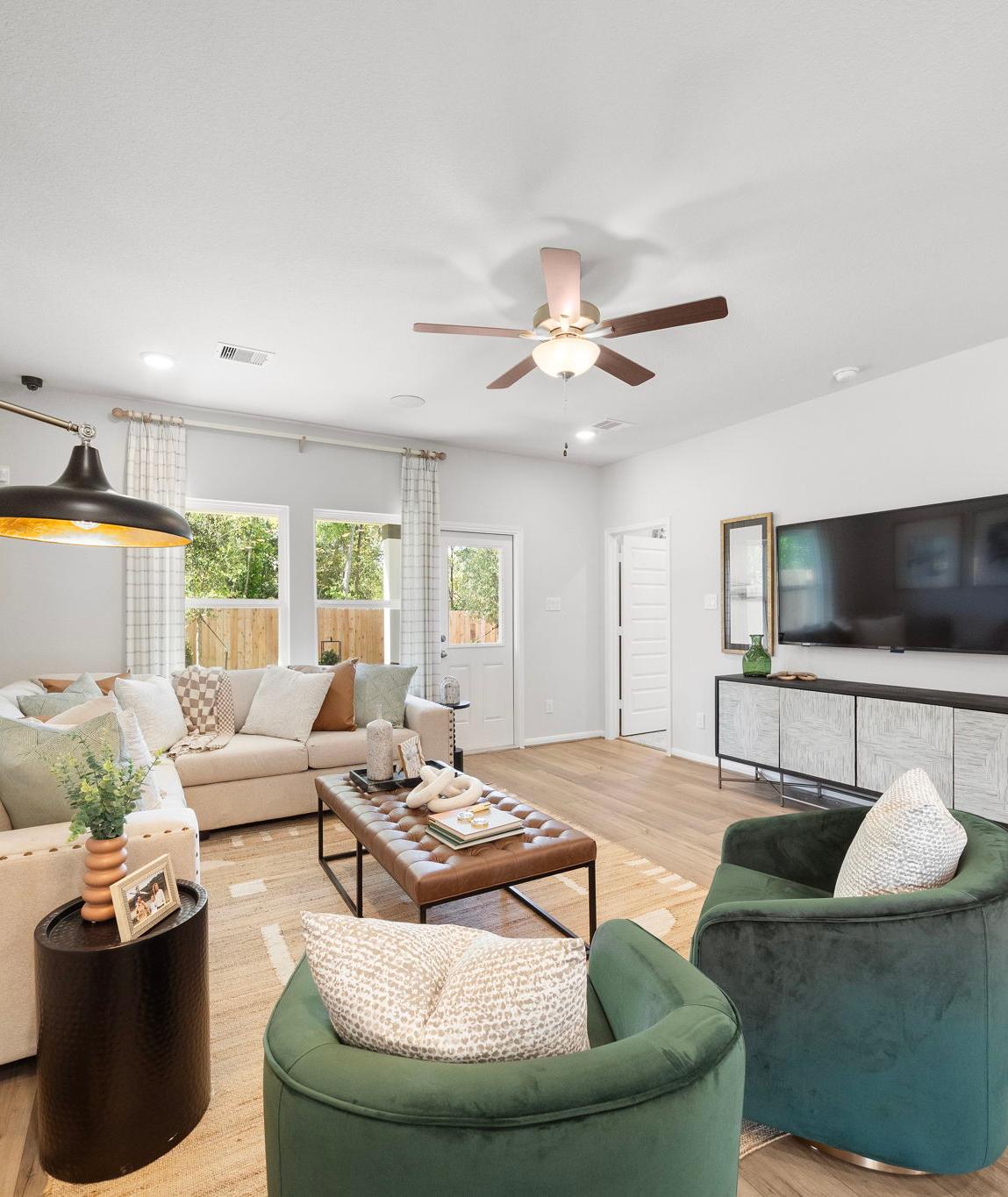 Spacious living room in Caney Creek Place Conroe TX with beige sectional sofa, emerald green velvet chairs, hardwood floors, ceiling fan, and modern art