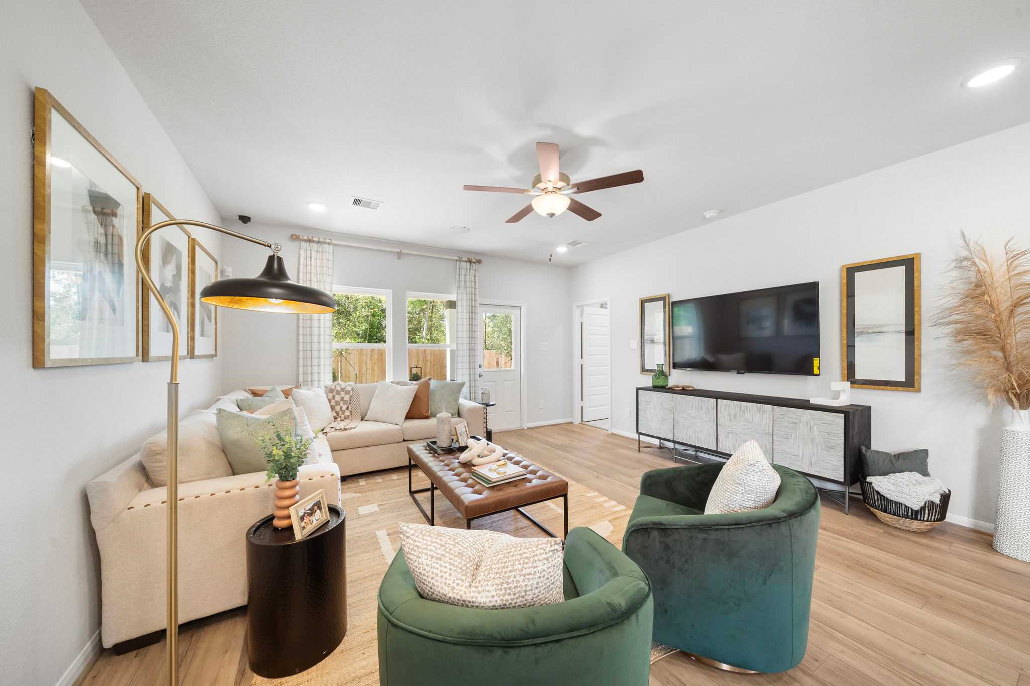 Spacious open-concept living room at Caney Creek Place in Conroe Texas with beige sofa, green velvet armchairs, hardwood floors and modern decor