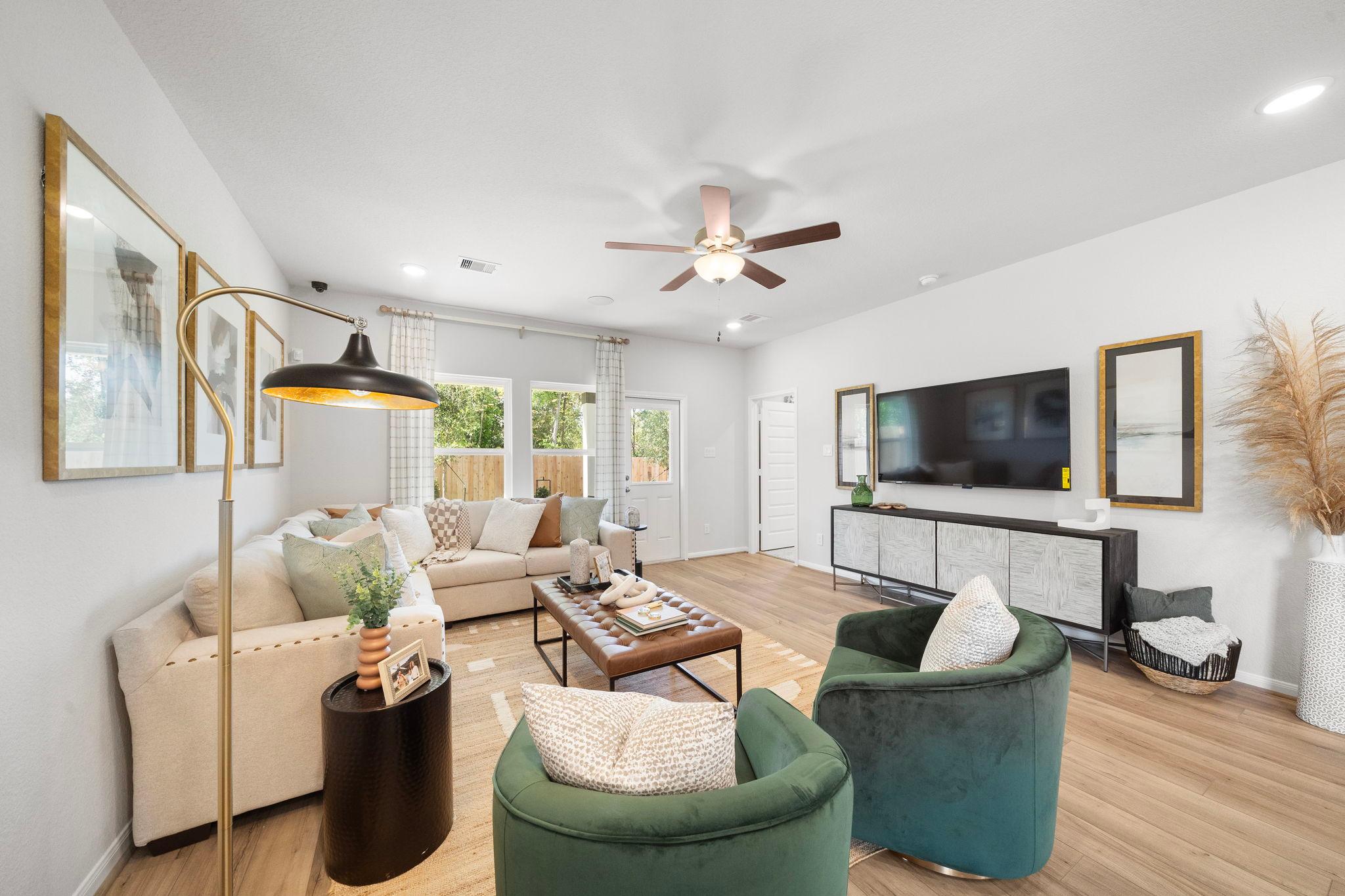 Spacious open-concept living room at Caney Creek Place in Conroe Texas with beige sofa, green velvet armchairs, hardwood floors and modern decor