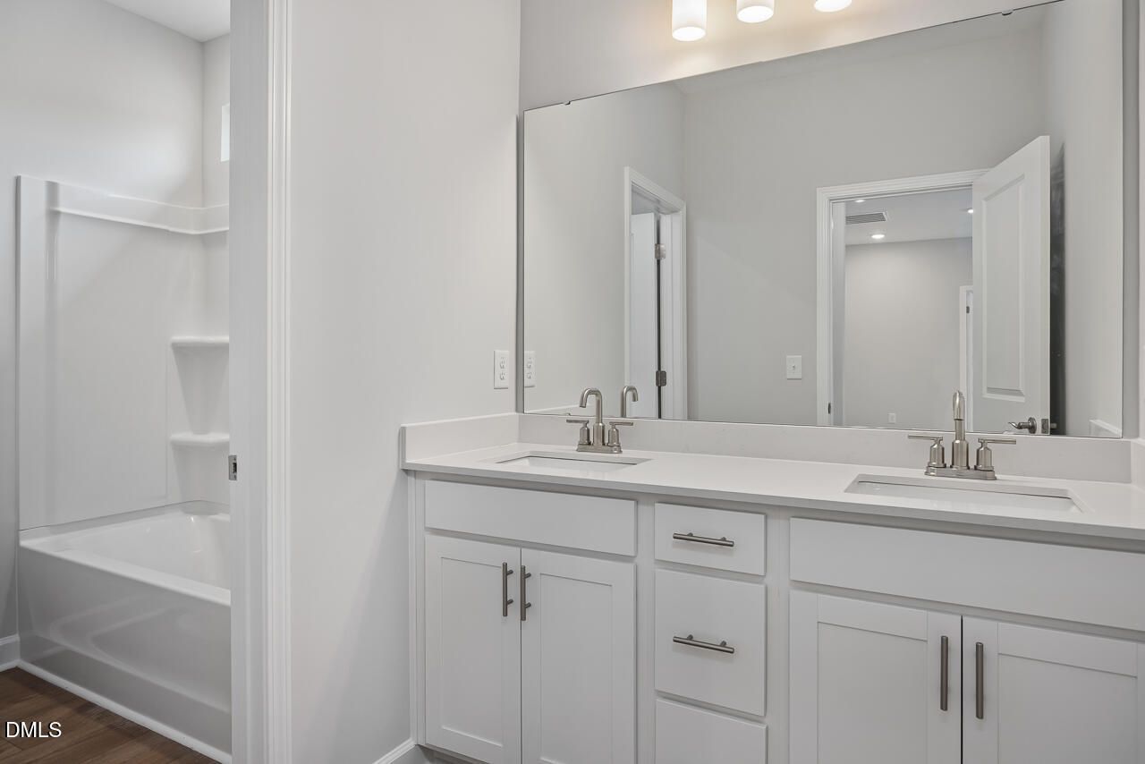 Modern bathroom with dual vanity, white cabinets, and tub-shower combo in The Ashport L at Sage on North Main, Wake Forest.