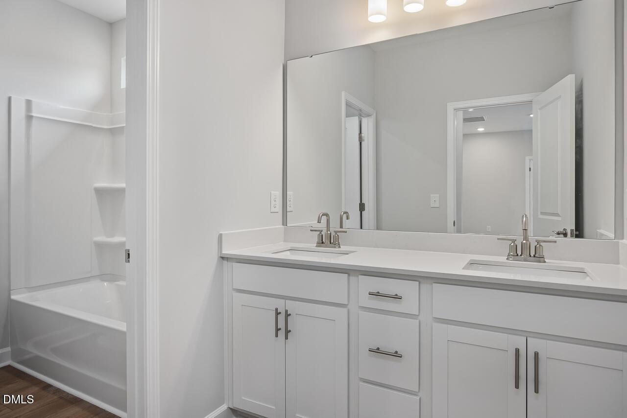 Modern bathroom with dual vanity, white cabinets, and tub-shower combo in The Ashport L at Sage on North Main, Wake Forest.