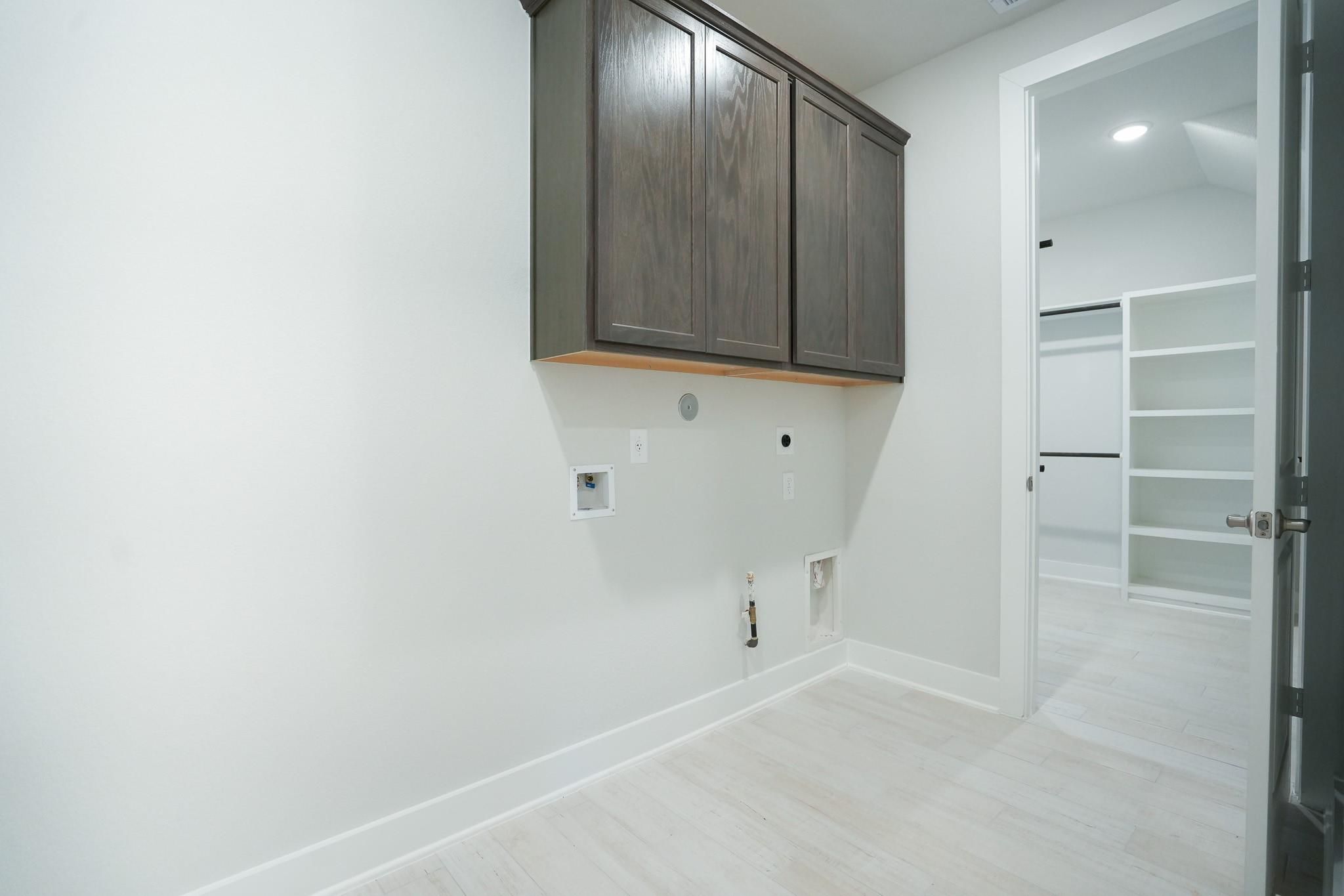 Modern laundry room with wooden cabinets, washer hookups, and open shelving in Davidson Homes The Edward C, Lago Mar, Texas City