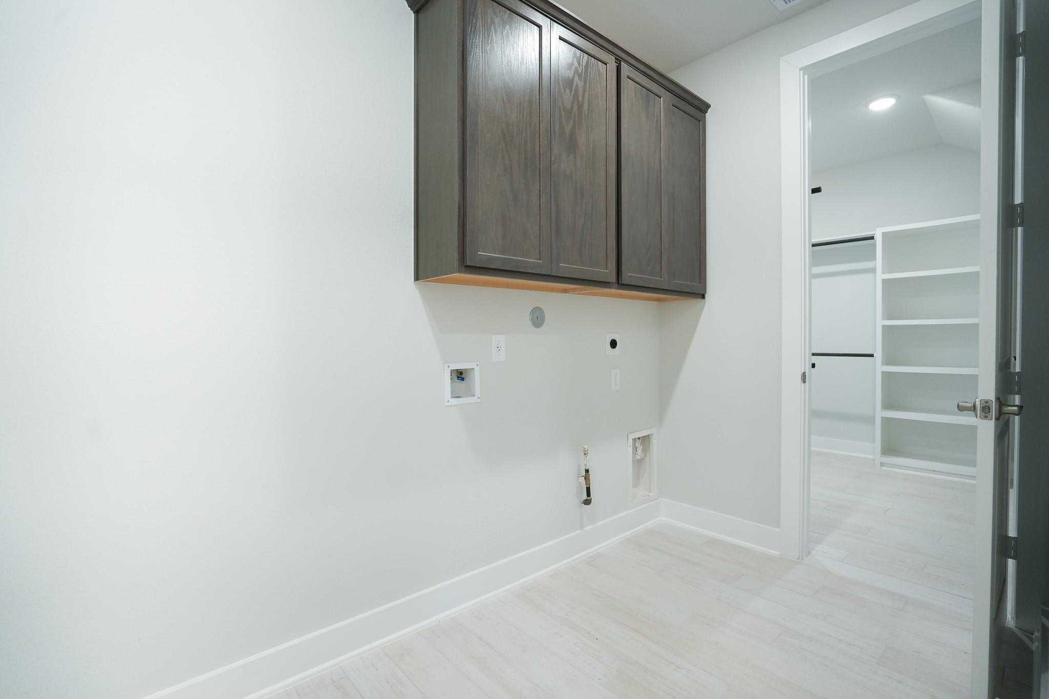 Modern laundry room with wooden cabinets, washer hookups, and open shelving in Davidson Homes The Edward C, Lago Mar, Texas City