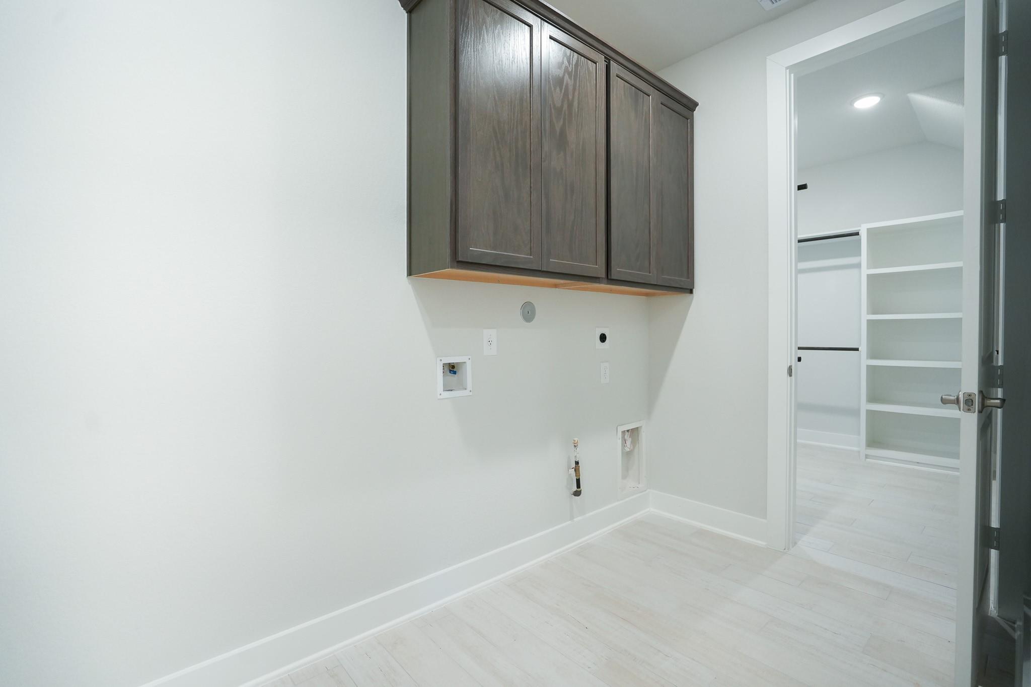 Modern laundry room with wooden cabinets, washer hookups, and open shelving in Davidson Homes The Edward C, Lago Mar, Texas City