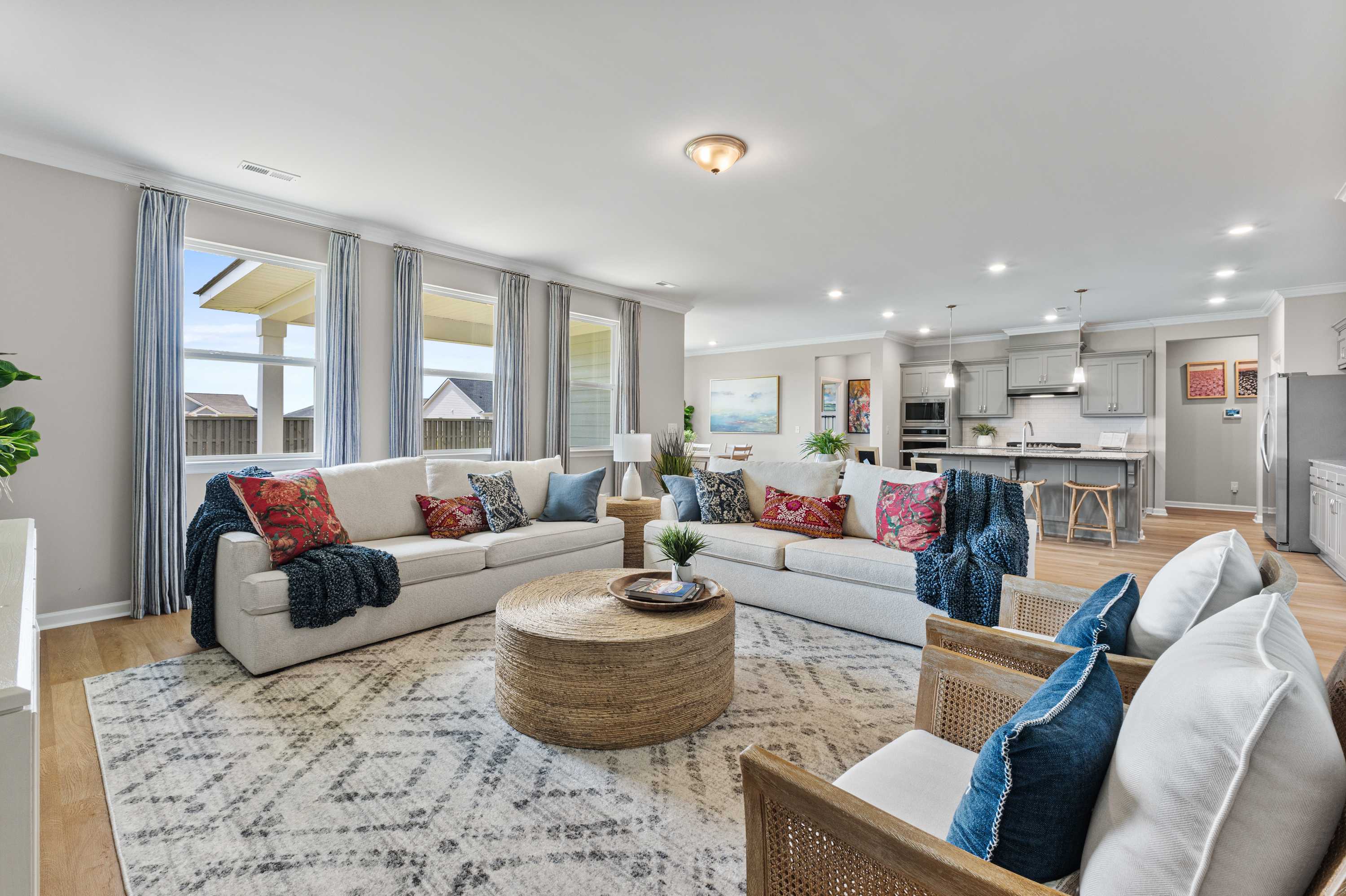 Spacious open-concept living room at The Meadows at Hampton Cove in Owens Cross Roads AL with neutral sofas, woven coffee table, and modern kitchen