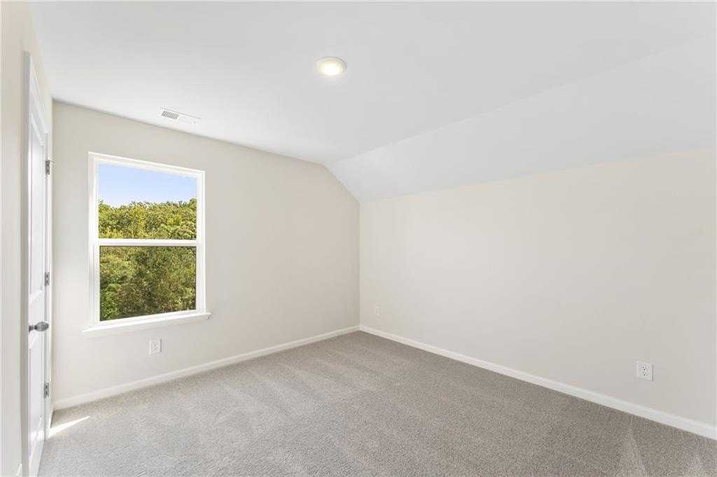 Bright secondary bedroom with vaulted ceiling, carpet flooring, and treetop view window in Davidson Homes The Ash B- Unfinished Basement, Riverwood, Dallas, Georgia
