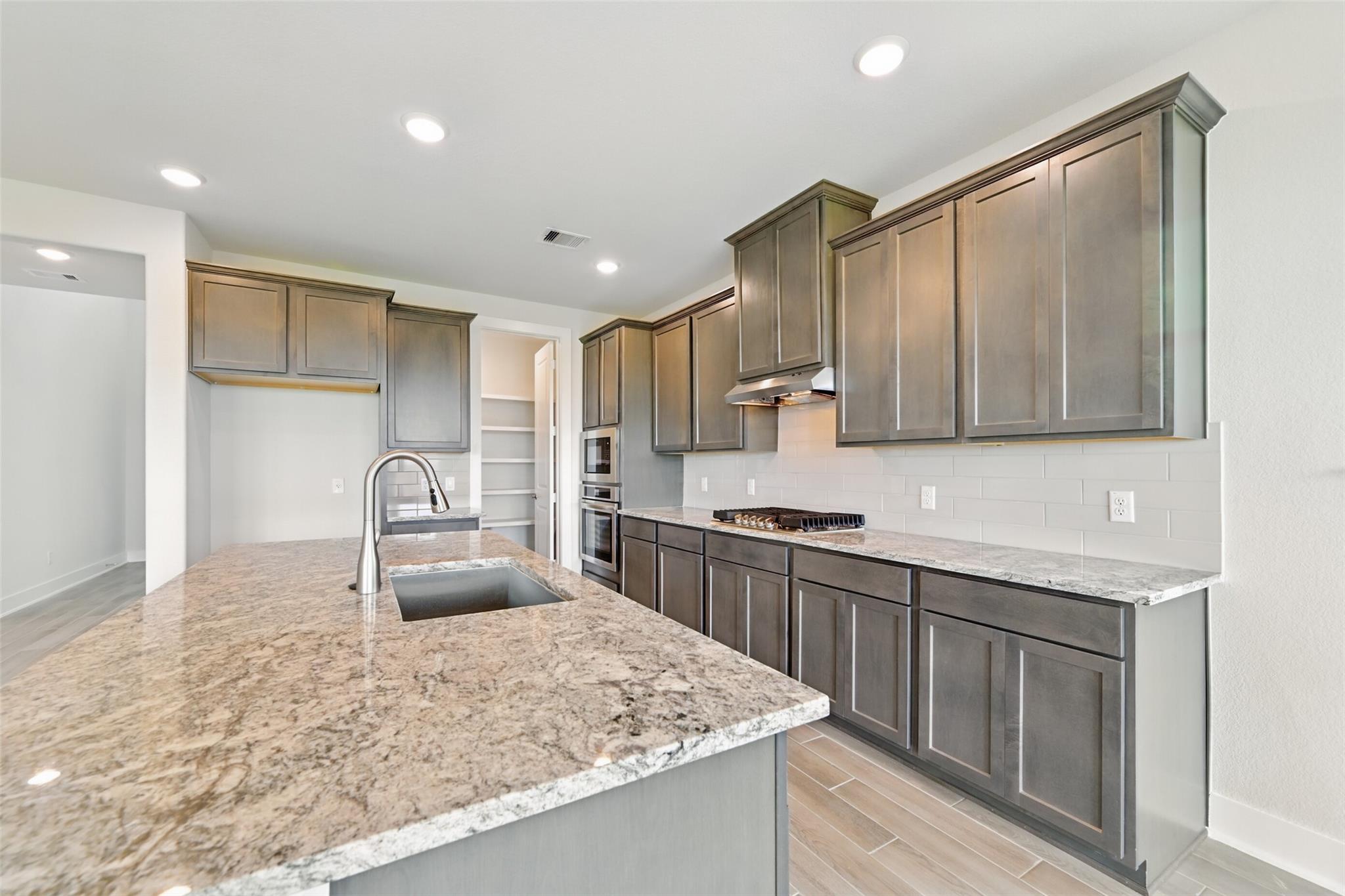 Modern gray shaker kitchen with granite countertops, stainless steel appliances, and island in Davidson Homes The Philip A, Lago Mar, Texas City