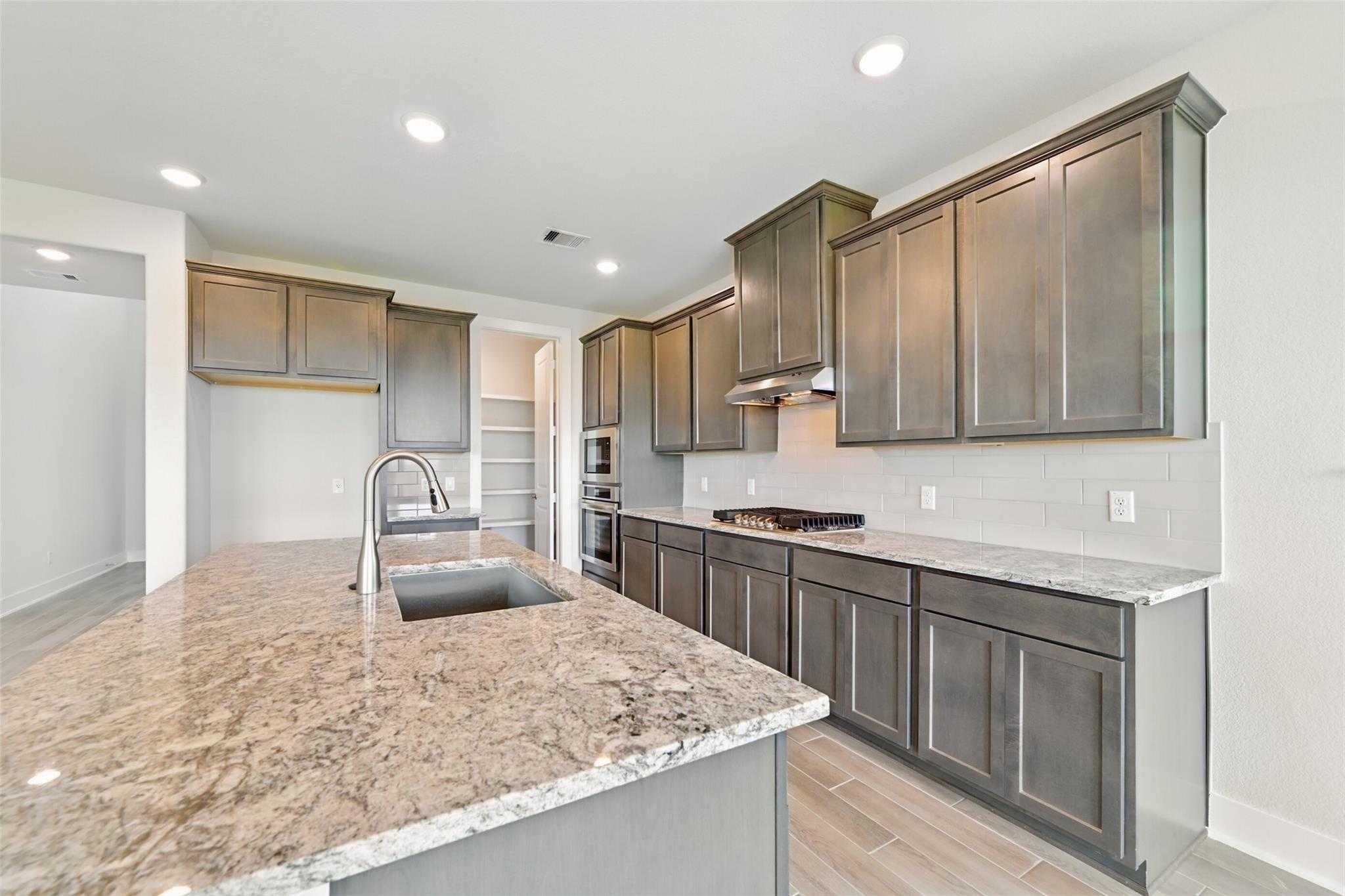 Modern gray shaker kitchen with granite countertops, stainless steel appliances, and island in Davidson Homes The Philip A, Lago Mar, Texas City
