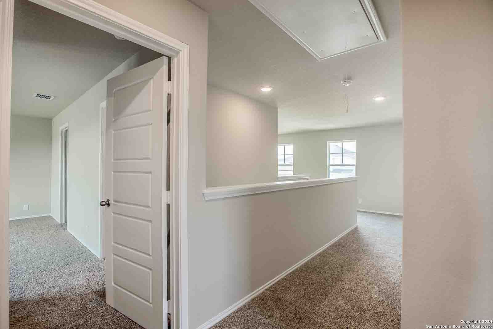 Upstairs hallway with beige walls, carpeted flooring, paneled doors, and overlook railing in Davidson Homes The Murray H, Seguin, Texas