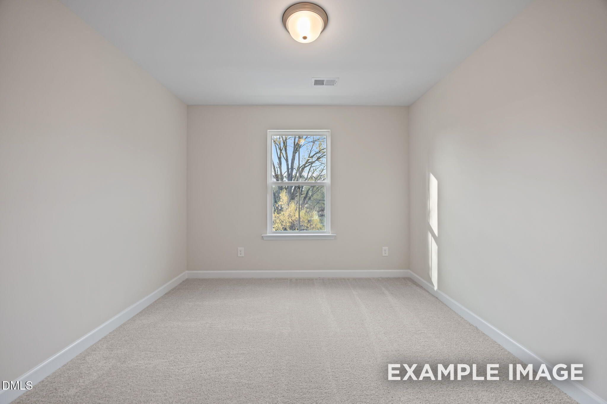 Empty bedroom with neutral beige walls, plush carpet floor, large window overlooking bare trees in Davidson Homes The Avery, Knightdale, NC