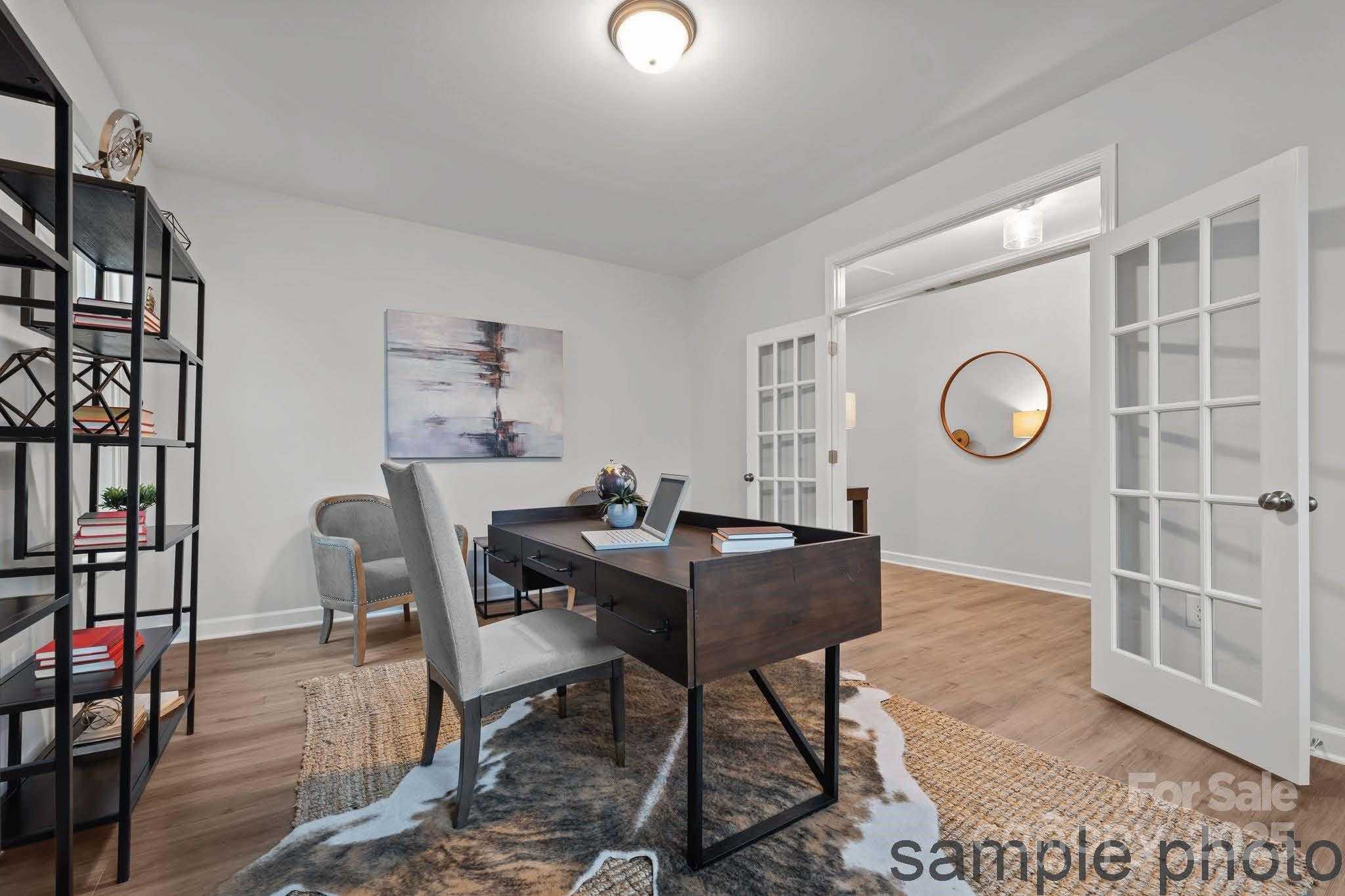 Modern home office with wooden desk, gray chair, black bookshelves, abstract art, and French doors in Davidson Homes Hickory E II, Belmont, NC