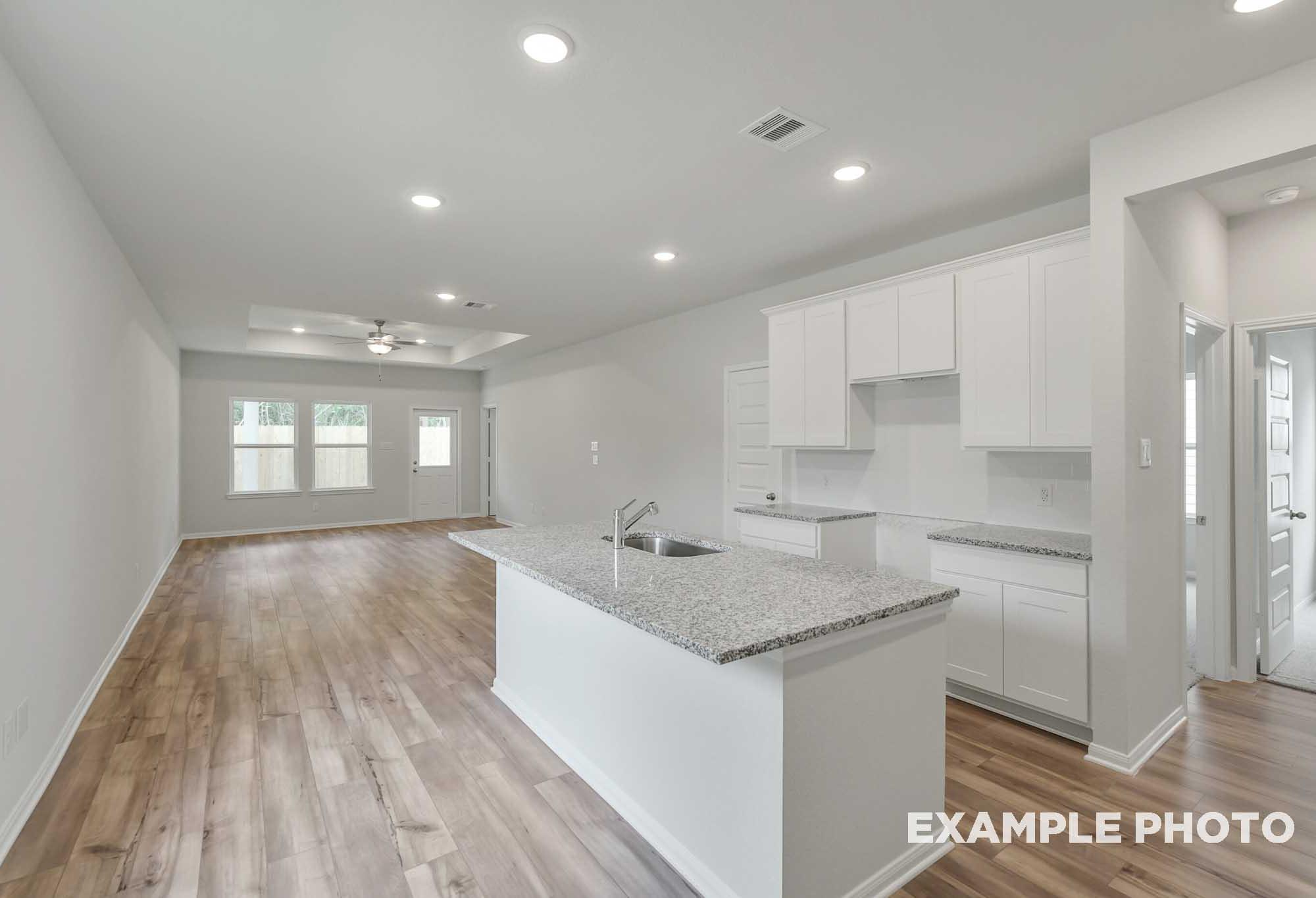 Open-concept kitchen and living area in The Frio floor plan featuring a granite island and wood-style flooring.