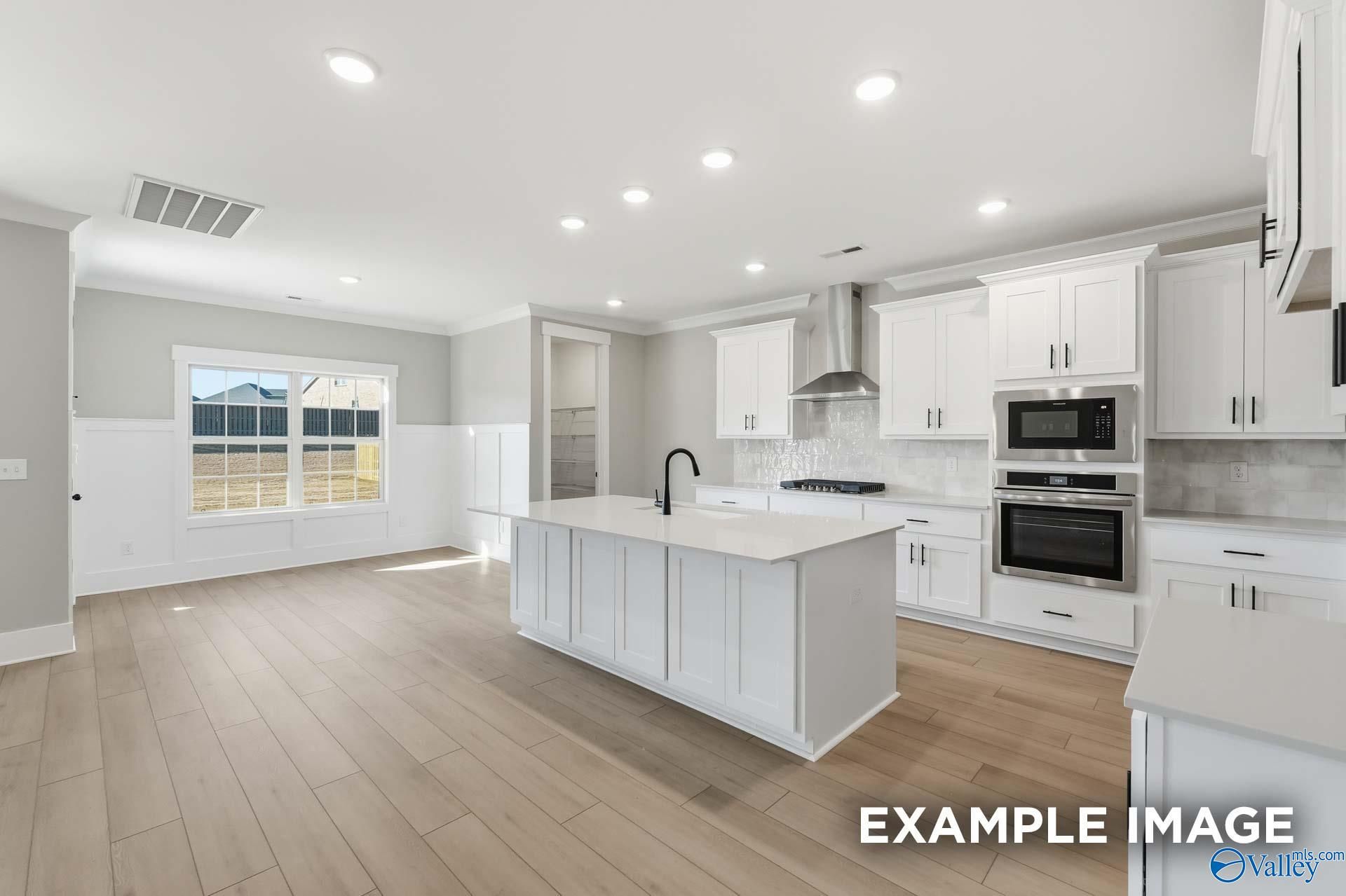 Modern open-concept kitchen with white shaker cabinets, large island, stainless appliances, and light oak floors in The Emory floor plan, Decatur, AL