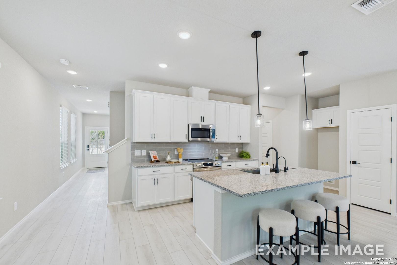 Modern white kitchen with quartz island, stainless appliances, and pendant lights in Davidson Homes The Charlotte B, San Antonio