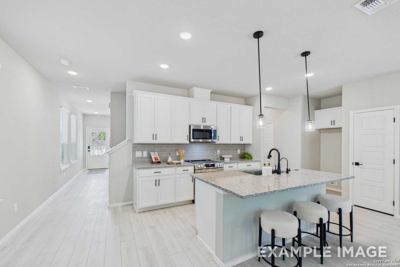Modern white kitchen with quartz island, stainless appliances, and pendant lights in Davidson Homes The Charlotte B, San Antonio