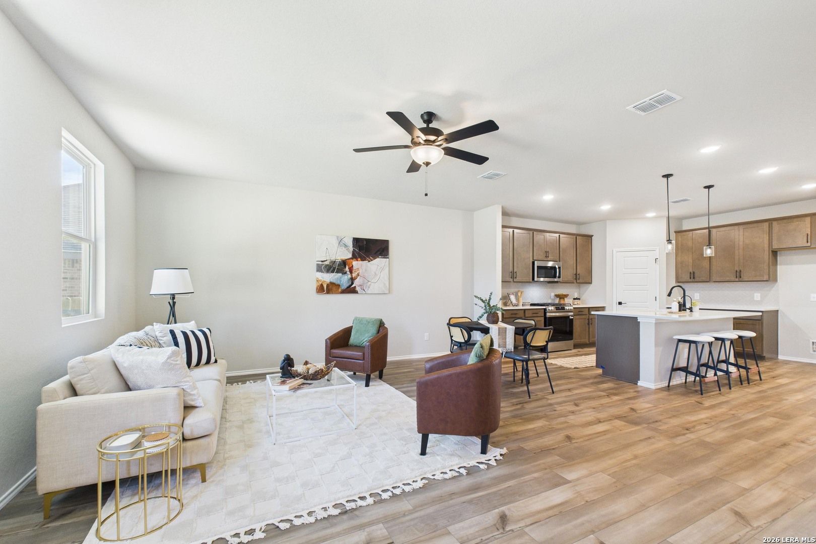 Open-concept living room and kitchen with beige sofa, ceiling fan, and modern island in Davidson Homes The Douglas E, San Antonio