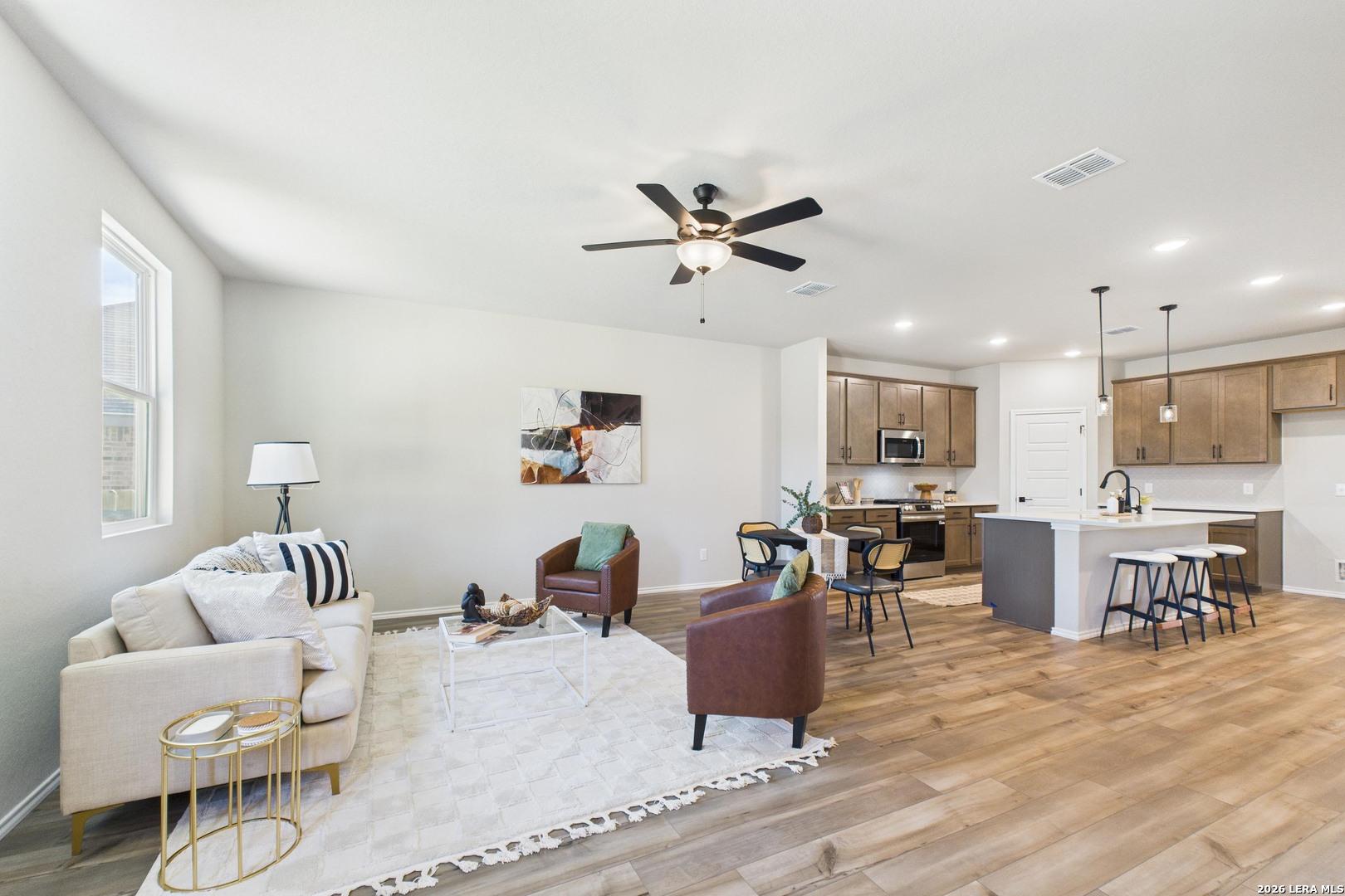 Open-concept living room and kitchen with beige sofa, ceiling fan, and modern island in Davidson Homes The Douglas E, San Antonio
