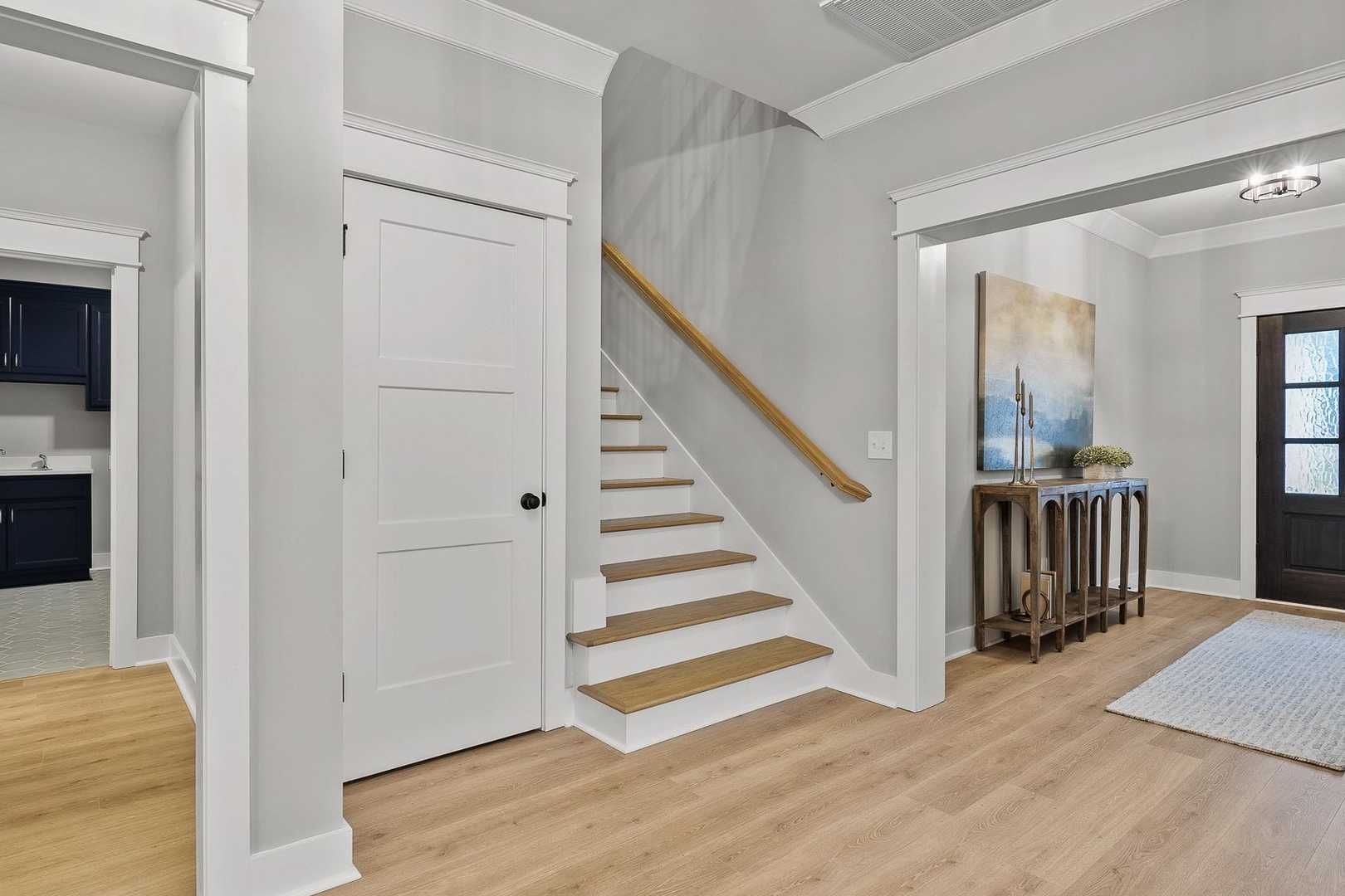 The Oxford home foyer with oak staircase, navy powder room, console table, and mahogany entry door