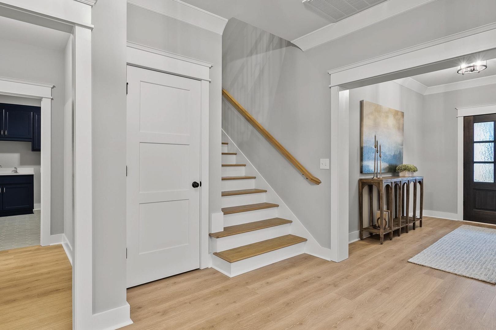 The Oxford home foyer with oak staircase, navy powder room, console table, and mahogany entry door