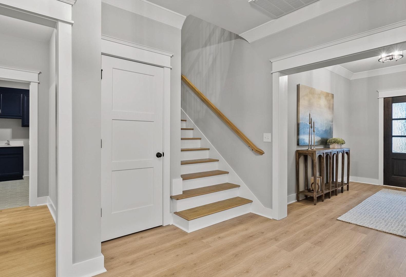 The Oxford home foyer with oak staircase, navy powder room, console table, and mahogany entry door